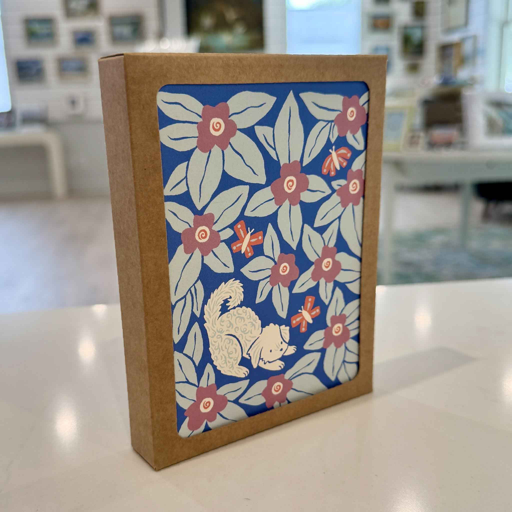 Nuthatch Studio Dogs & Blooms Greeting Card Boxed Set displayed inside Gray Man Gallery in Pawleys Island, South Carolina. This eco-friendly boxed set includes eight assorted greeting cards featuring whimsical dog and floral illustrations by Chrissie Van Hoever, printed on premium 100% recycled paper with matching recycled kraft envelopes and packaged in a keepsake kraft box.