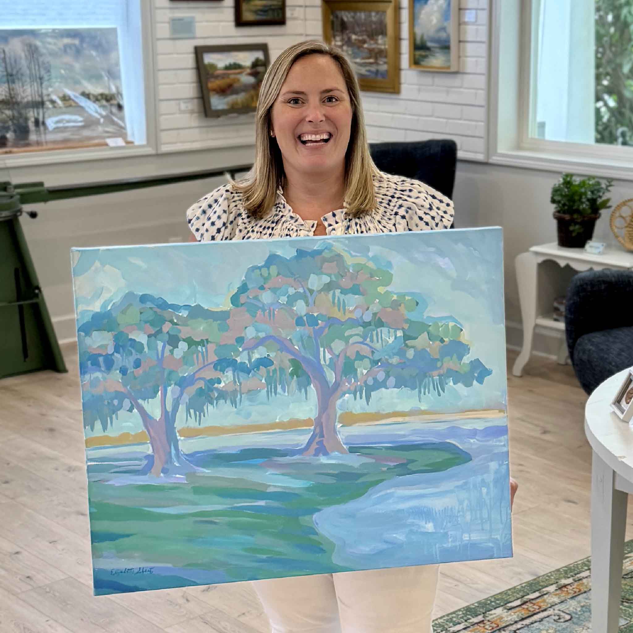 Bordy holding Live Oak Diptych I original acrylic painting by Elizabeth Sheats inside Gray Man Gallery showing scale of the gallery wrapped canvas with live oak trees and coastal Lowcountry landscape