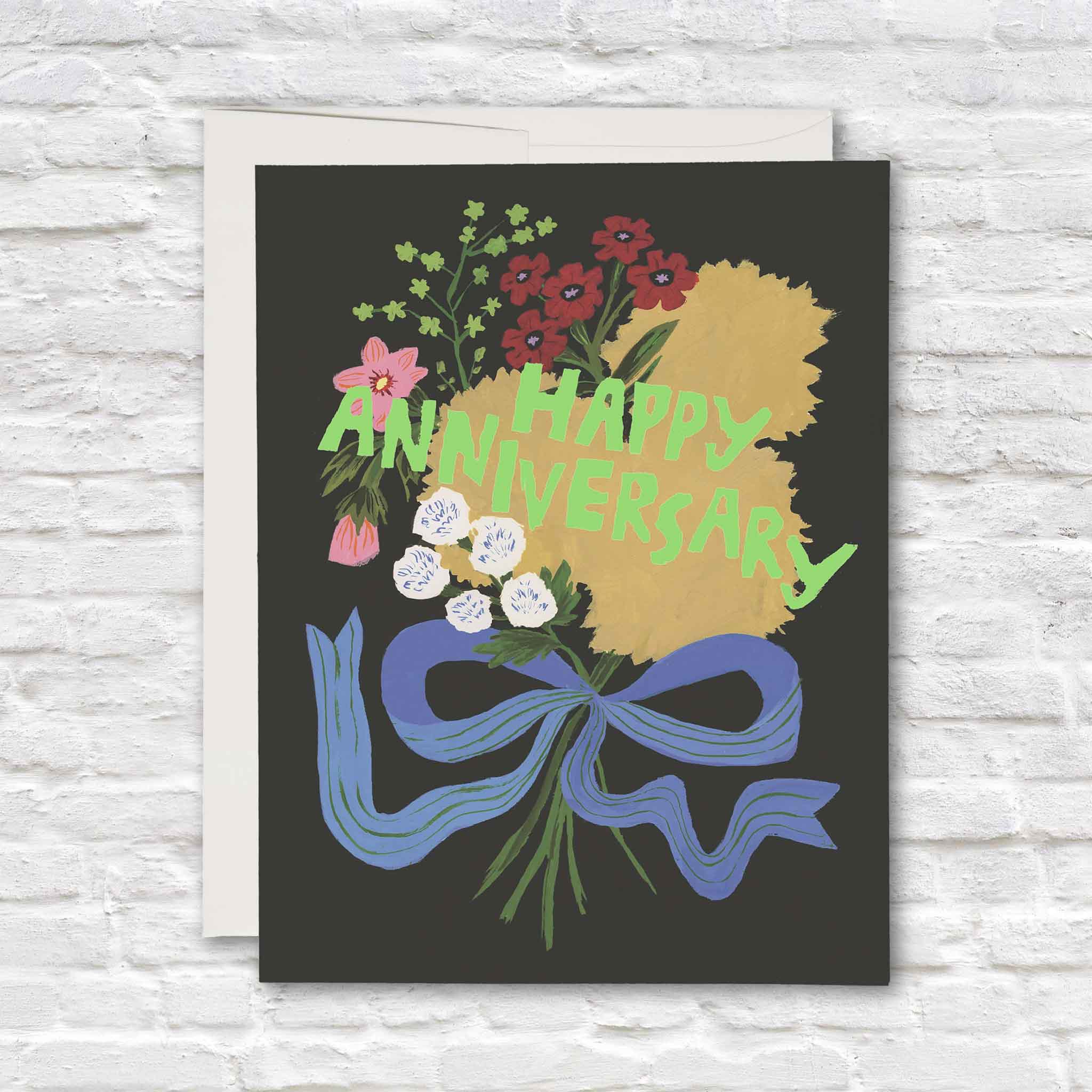 Anniversary Bouquet greeting card illustrated by Emily Isabella, featuring a colorful hand-painted bouquet of red, yellow, pink and white flowers tied with an oversized blue ribbon against a dark charcoal background, with bright green Happy Anniversary lettering, available at Gray Man Gallery in Pawleys Island, South Carolina.