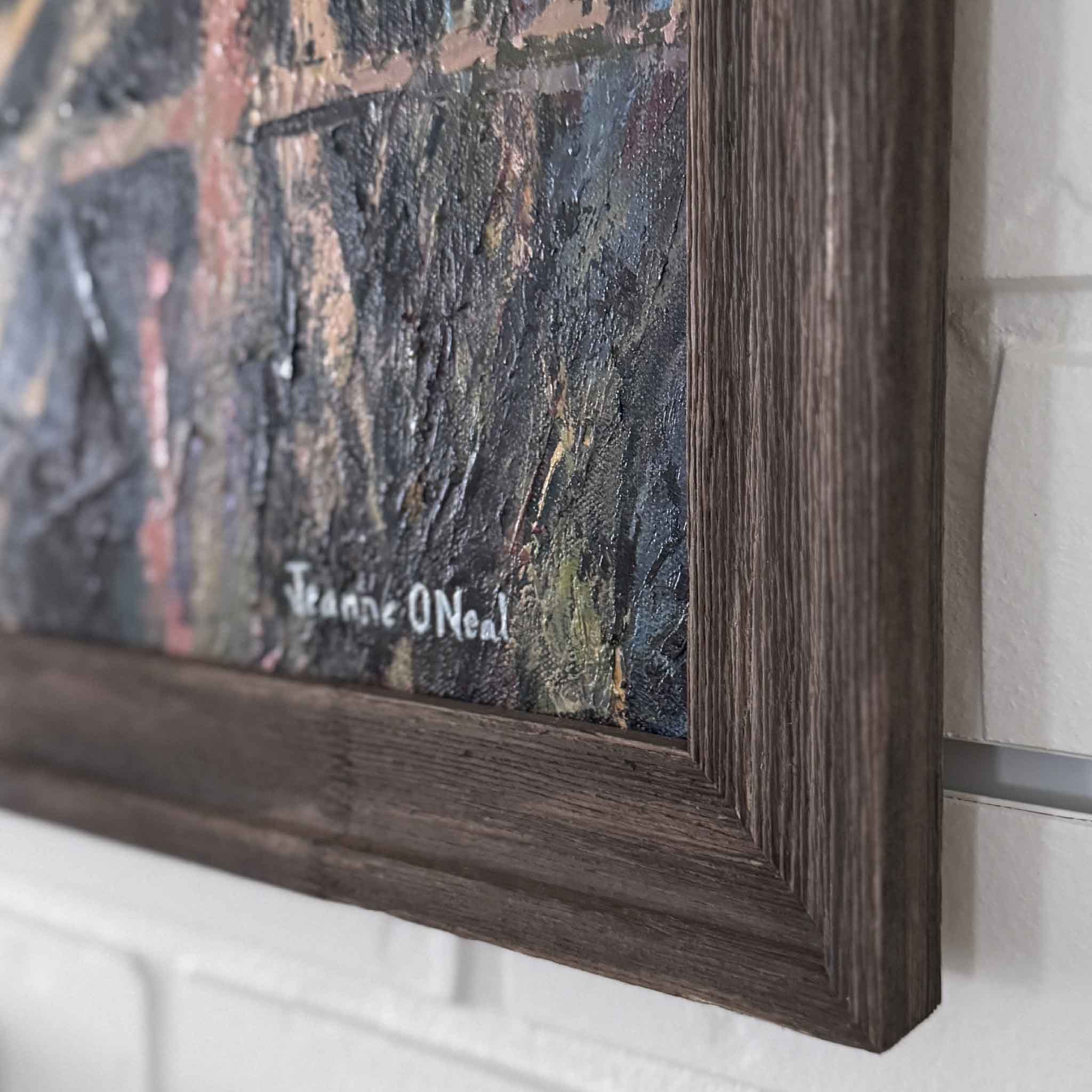 Close-up of a painting with a dark wooden frame and visible signature on a light-colored wall.