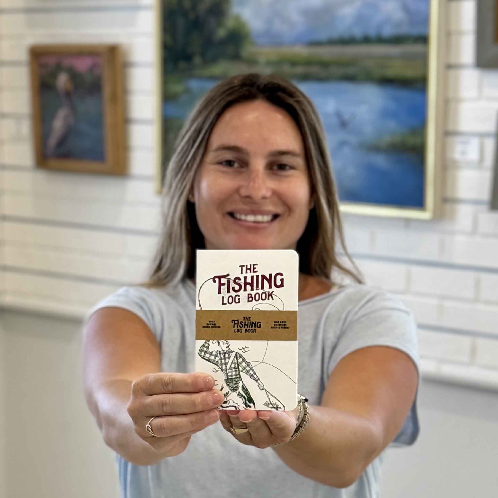 The Fishing Log Book available at Gray Man Gallery in Pawleys Island, South Carolina, shown in hand. Pocket-sized fishing journal for tracking catches, fishing trips, bait, weather, and memorable days on the water.