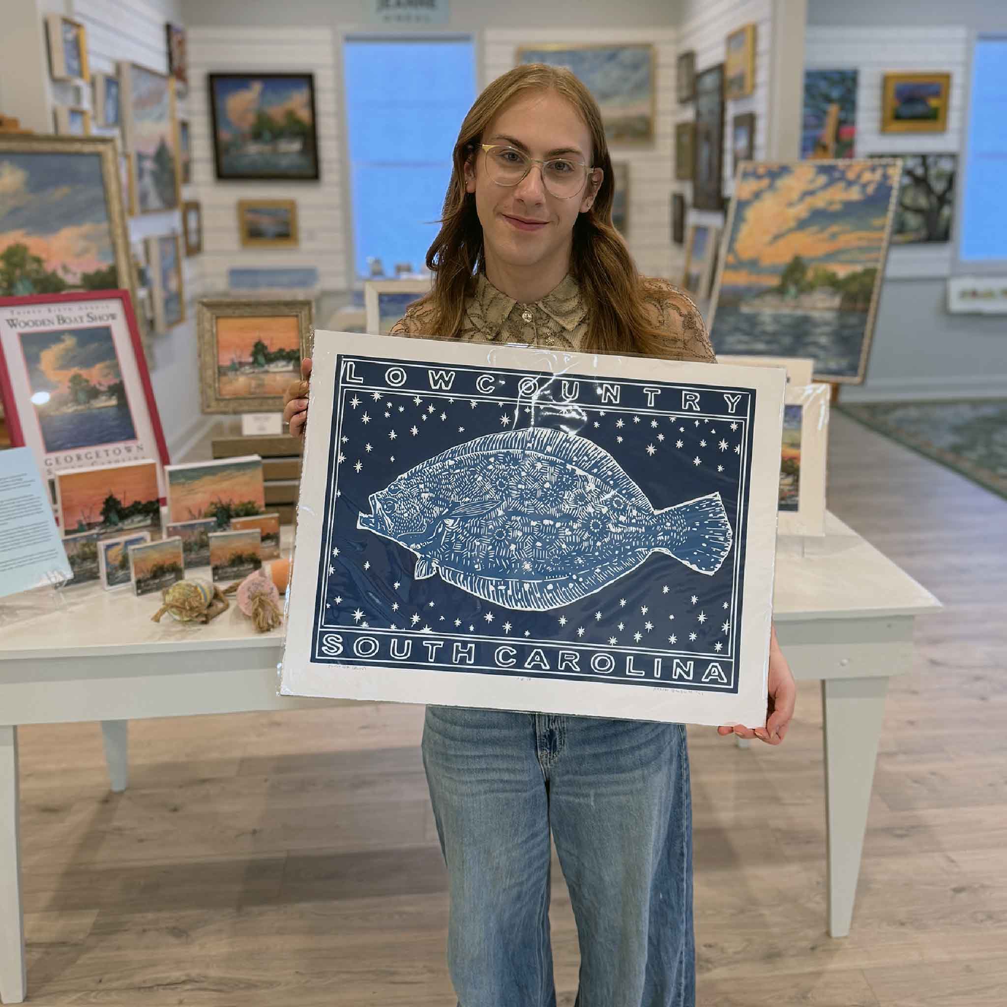 Alex holding the blue Flounder linocut print by Aaron Baldwin inside Gray Man Gallery.