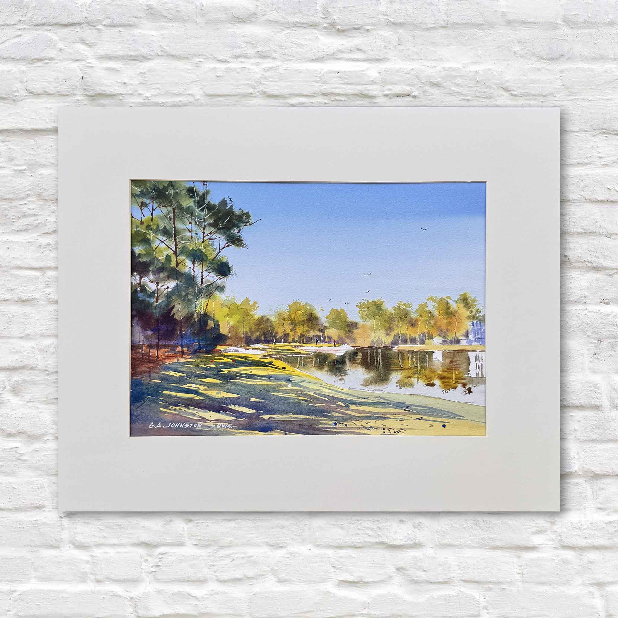 long afternoon shadows stretching across a grassy green beside calm reflective water, framed by trees and soft sky, matted to fit a standard 16x20 frame like those offered at Gray Man Gallery and photographed against a white gallery wall to highlight color, depth, and composition