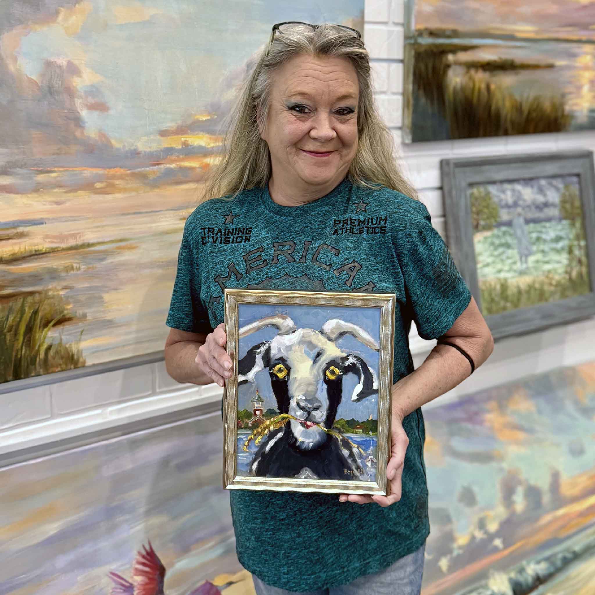 Gray Man Gallery team member holding an 8x10 framed goat painting by Jenny Reynolds for scale, inside the art gallery.