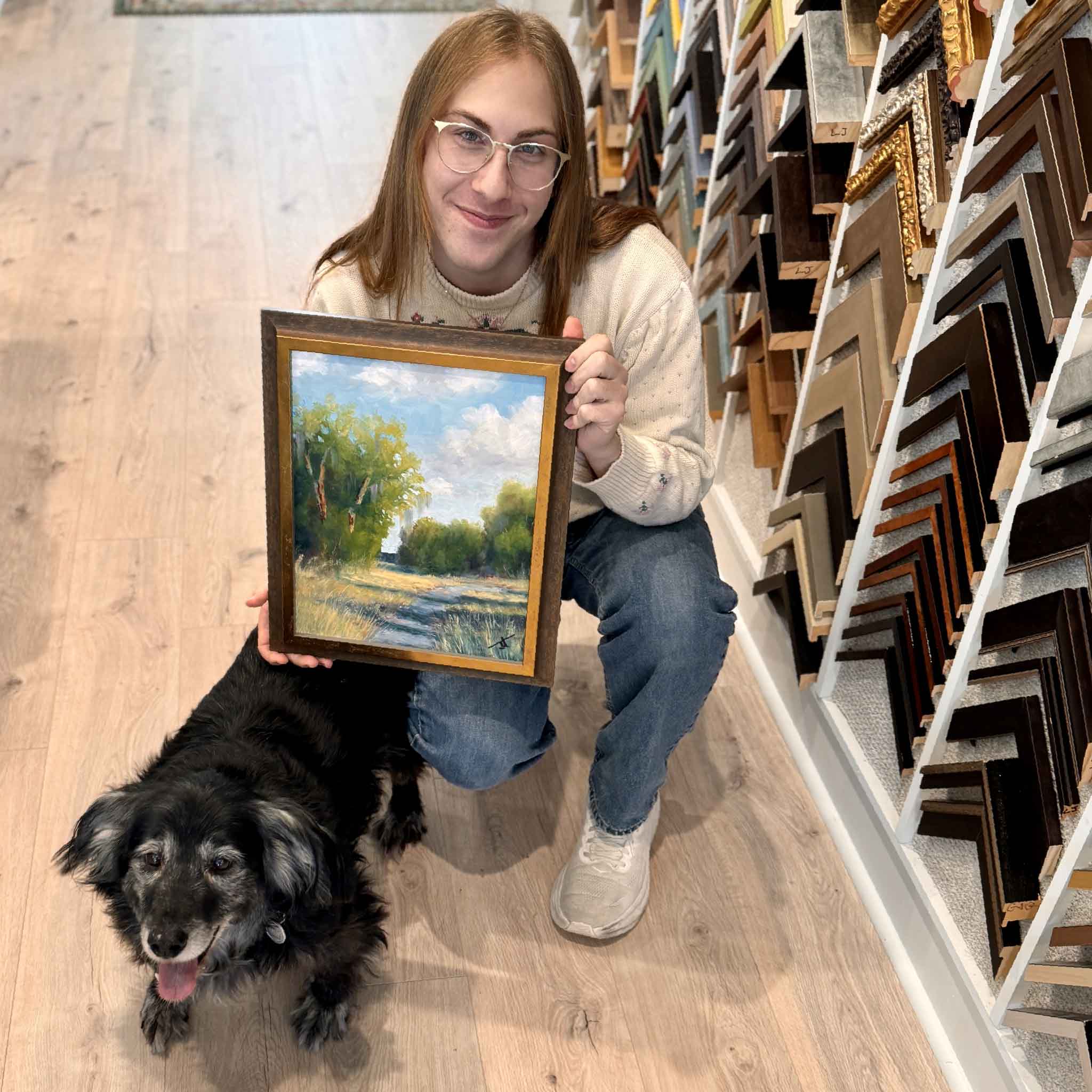 Jamie Arnold’s original oil painting Light Finds a Way shown held in the gallery for scale, demonstrating the framed 11x14 size in a real space. Also shown: Buddy, our rescue pup from Senior Dogs Senior Rescue.