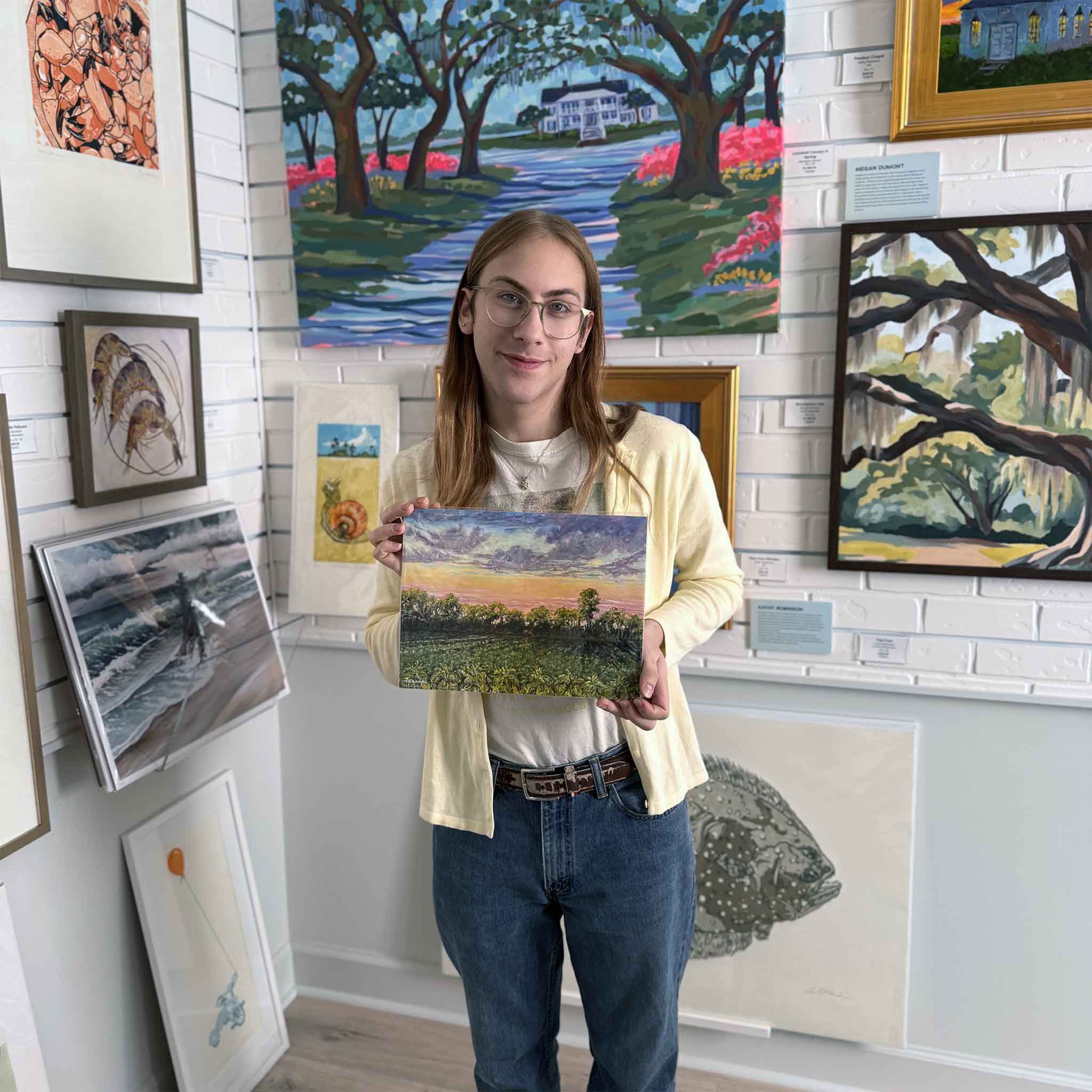 Alex holding Artist Jeanne O’Neal's Tobacco Fields fine art giclée print inside Gray Man Gallery, shown for scale to highlight the artwork’s size, color, and presence, and to provide context for how this Lowcountry landscape print appears in a gallery setting.