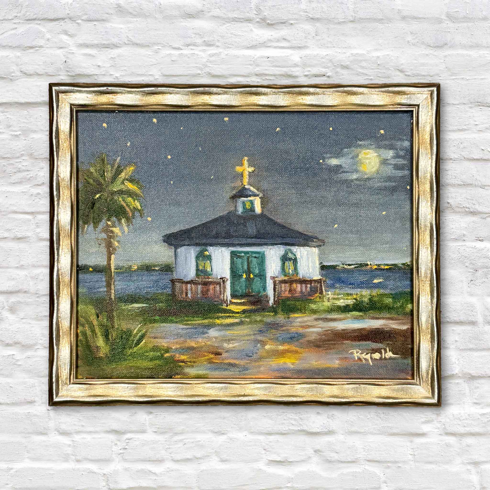 Moonlight Over the Chapel by Jenny Reynolds is an original oil painting featuring a small coastal chapel beneath a glowing full moon, with stars overhead, shimmering water, and a palmetto tree framing the peaceful Lowcountry scene. Professionally framed in Jenny Reynolds' signature champagne frame and available at Gray Man Gallery in Pawleys Island, South Carolina.