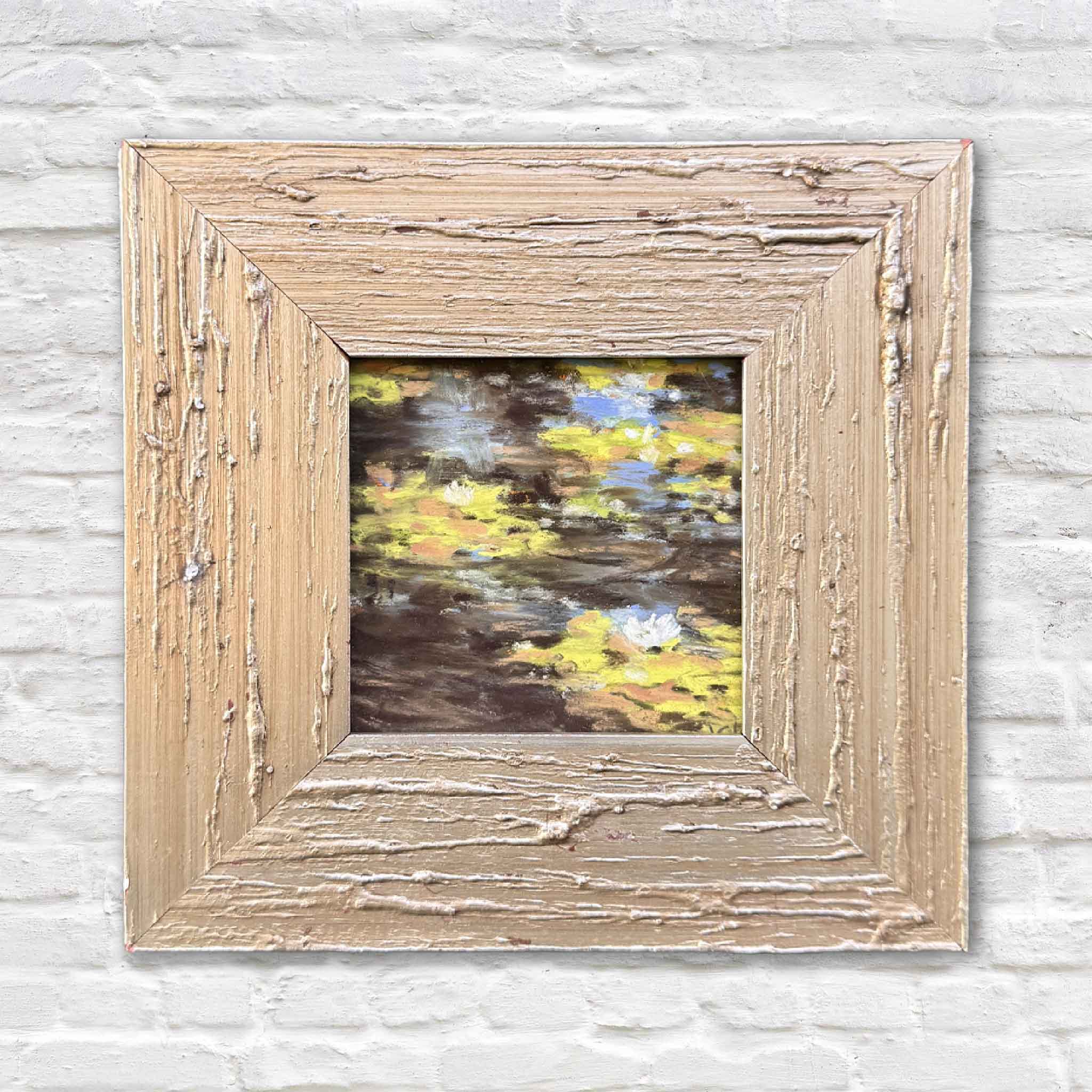 Lilies I is an original framed pastel by Lowcountry artist Joanne Willoughby, featuring soft golden reflections and lily-inspired forms floating across dark water, presented in a rustic wood frame at Gray Man Gallery in Pawleys Island, South Carolina.