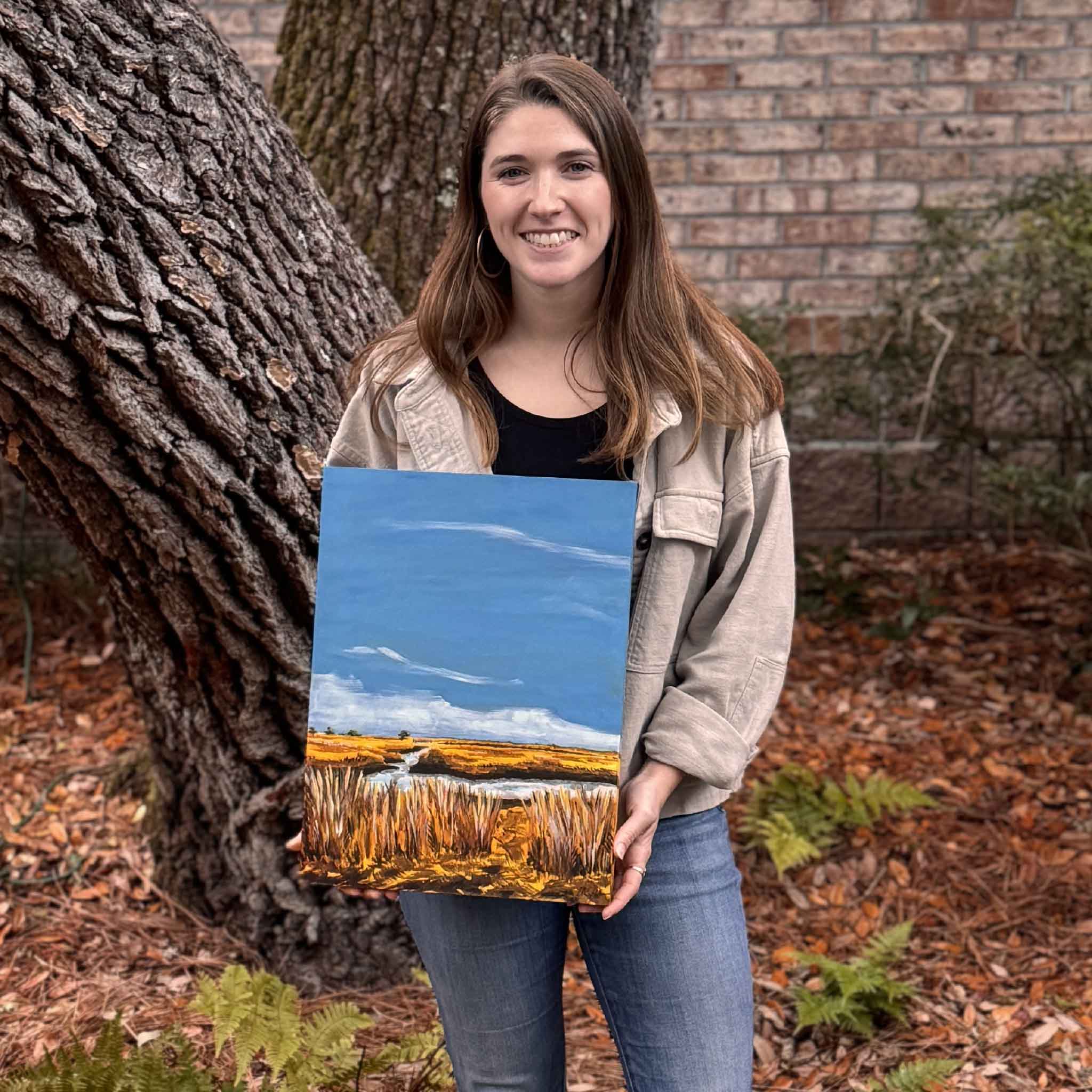 Artist Maggie Pelton holding her original 12 x 16 acrylic painting Autumn Sun at Clambank outdoors, shown for scale and photographed for Gray Man Gallery.