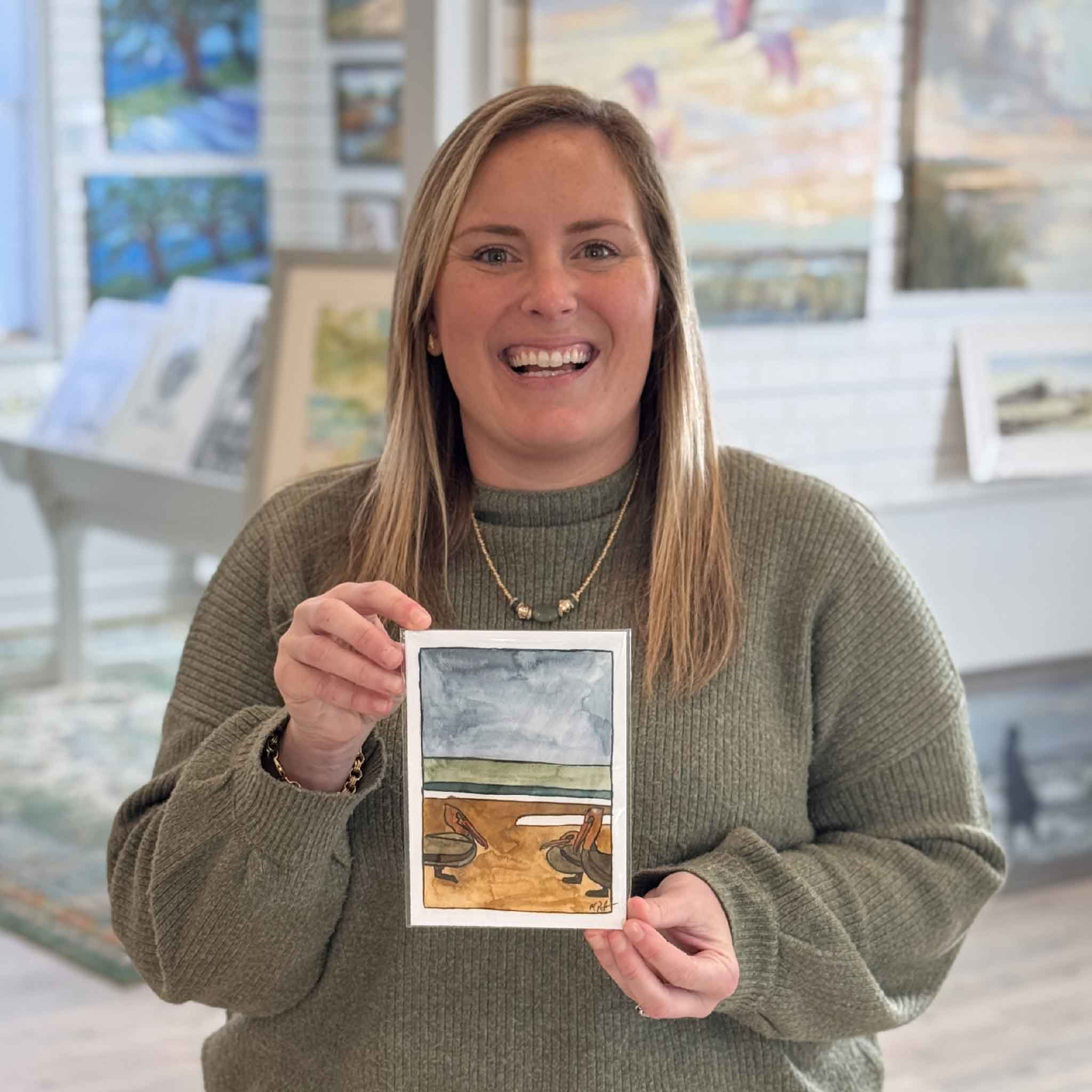 Bordy holding local artist Maggie Pelton's 5 x 7 giclée print Pelican outdoors, shown for scale and photographed in the courtyard at Gray Man Gallery.