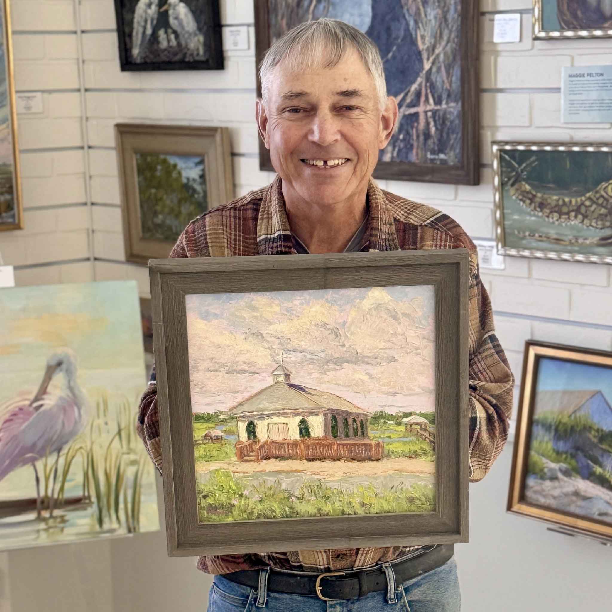 Local artist Michael Rogan holding his original oil painting of the Pawleys Island Chapel, professionally framed and displayed at Gray Man Gallery in Pawleys Island, South Carolina.