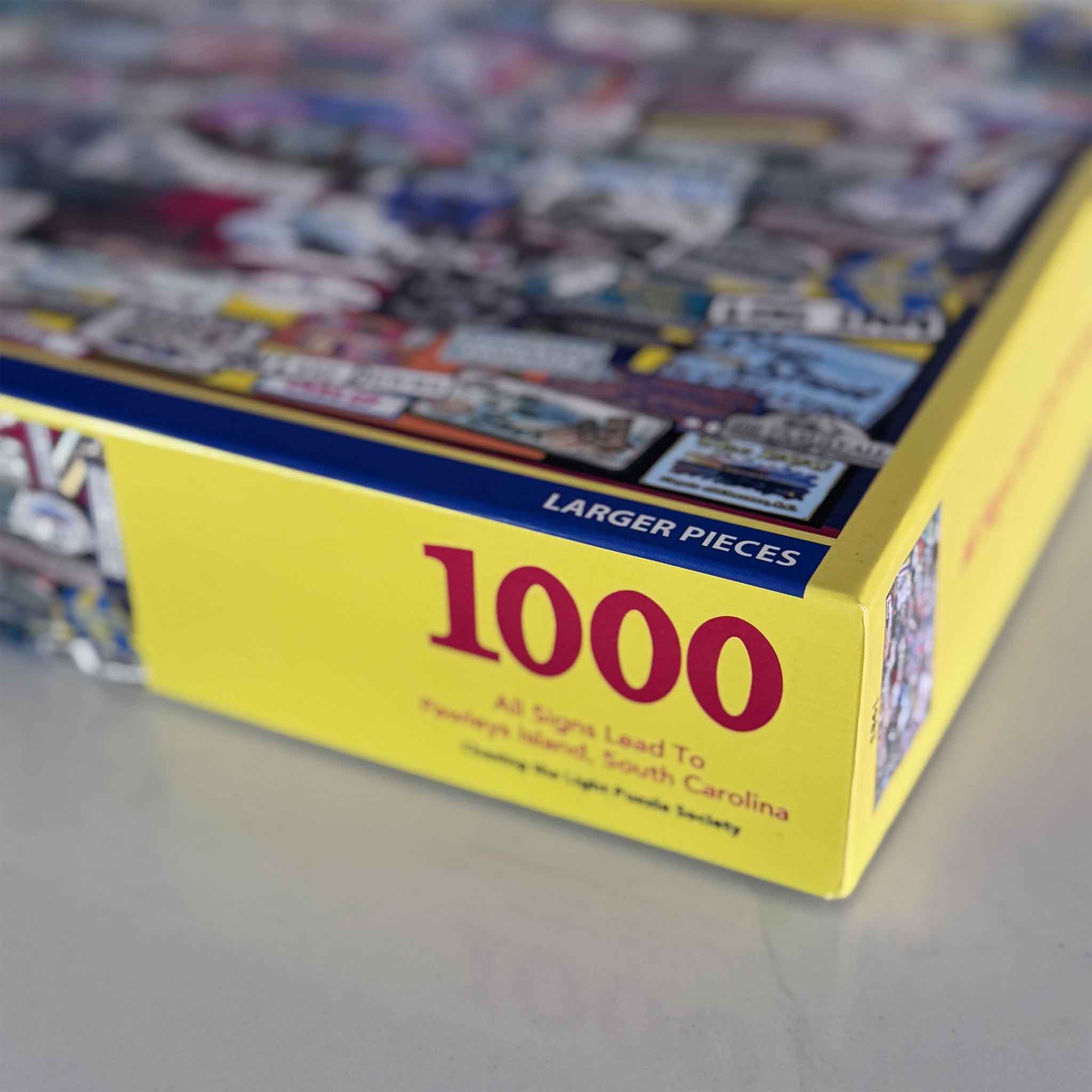 Close-up of the All Signs Lead to Pawleys Island 1,000-piece puzzle box by Tanya Ackerman, showing larger puzzle pieces and colorful sign artwork.