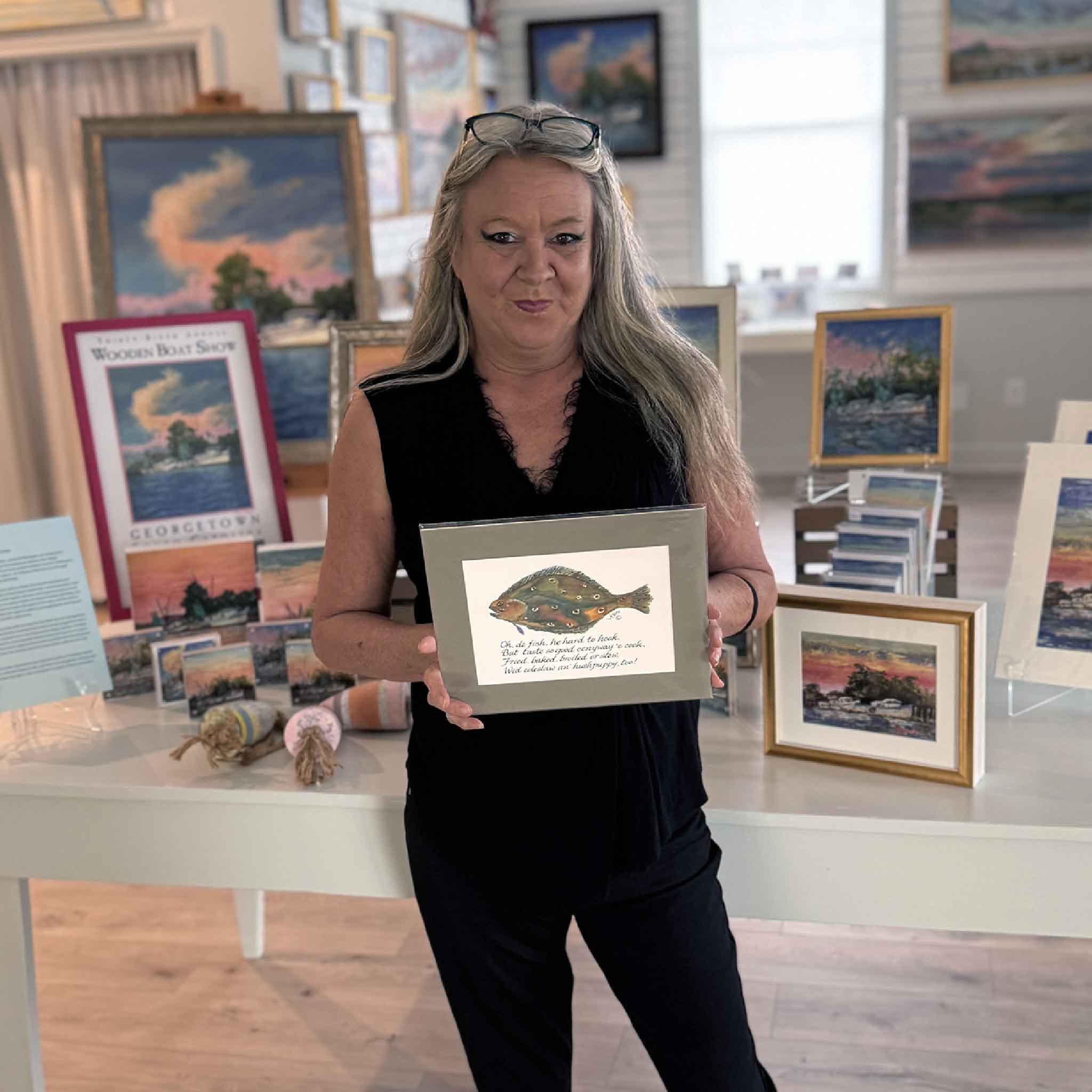 Charlotte holding Gullah Odes Flounder by Vida Miller, a matted watercolor print featuring a whimsical flounder with a hand-lettered Gullah-style verse, shown with a beige mat, inspired by Lowcountry seafood traditions.