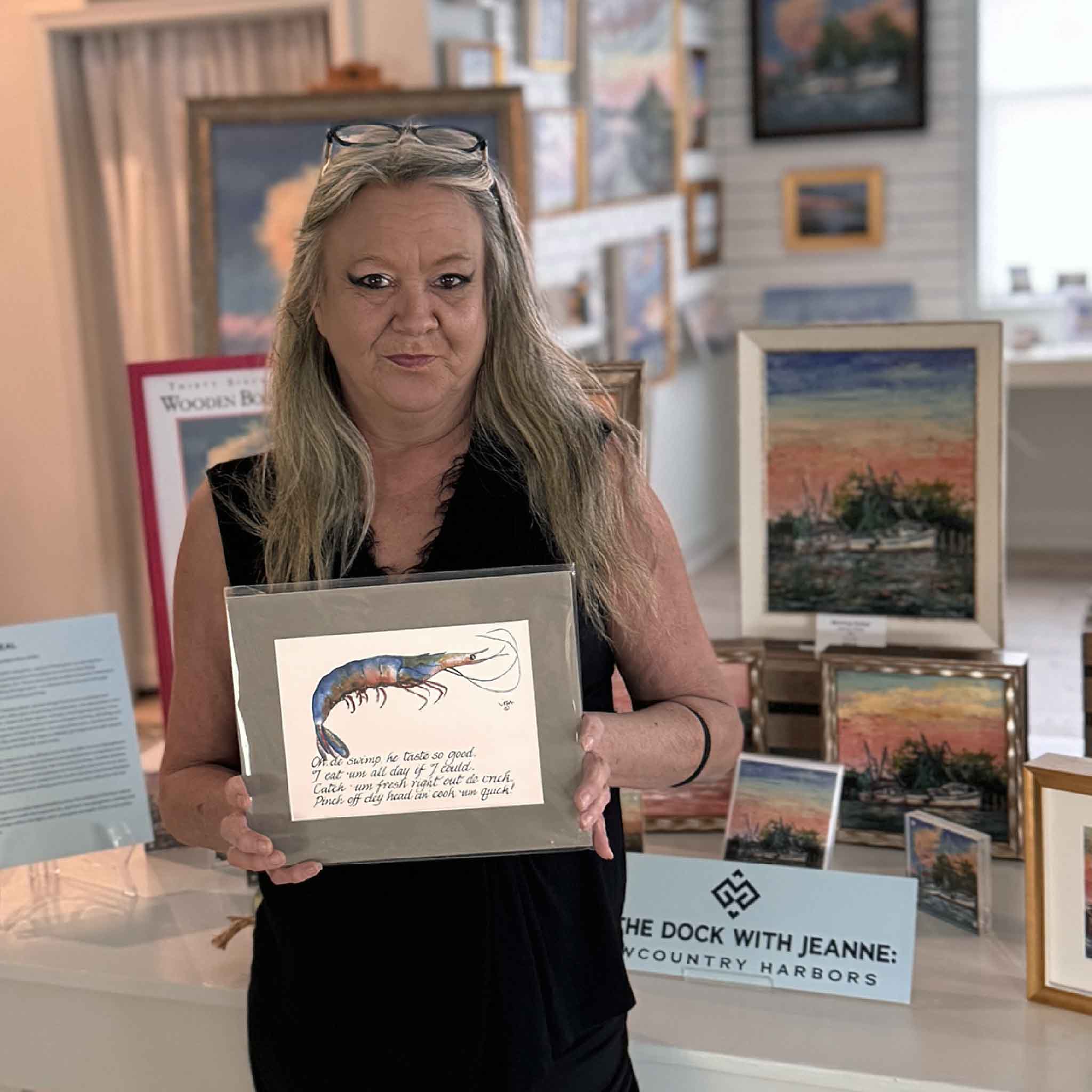 Gallery lifestyle photo showing a person holding the Gullah Odes: Shrimp matted print by Vida Miller, illustrating scale and showcasing the artwork in a coastal gallery setting.