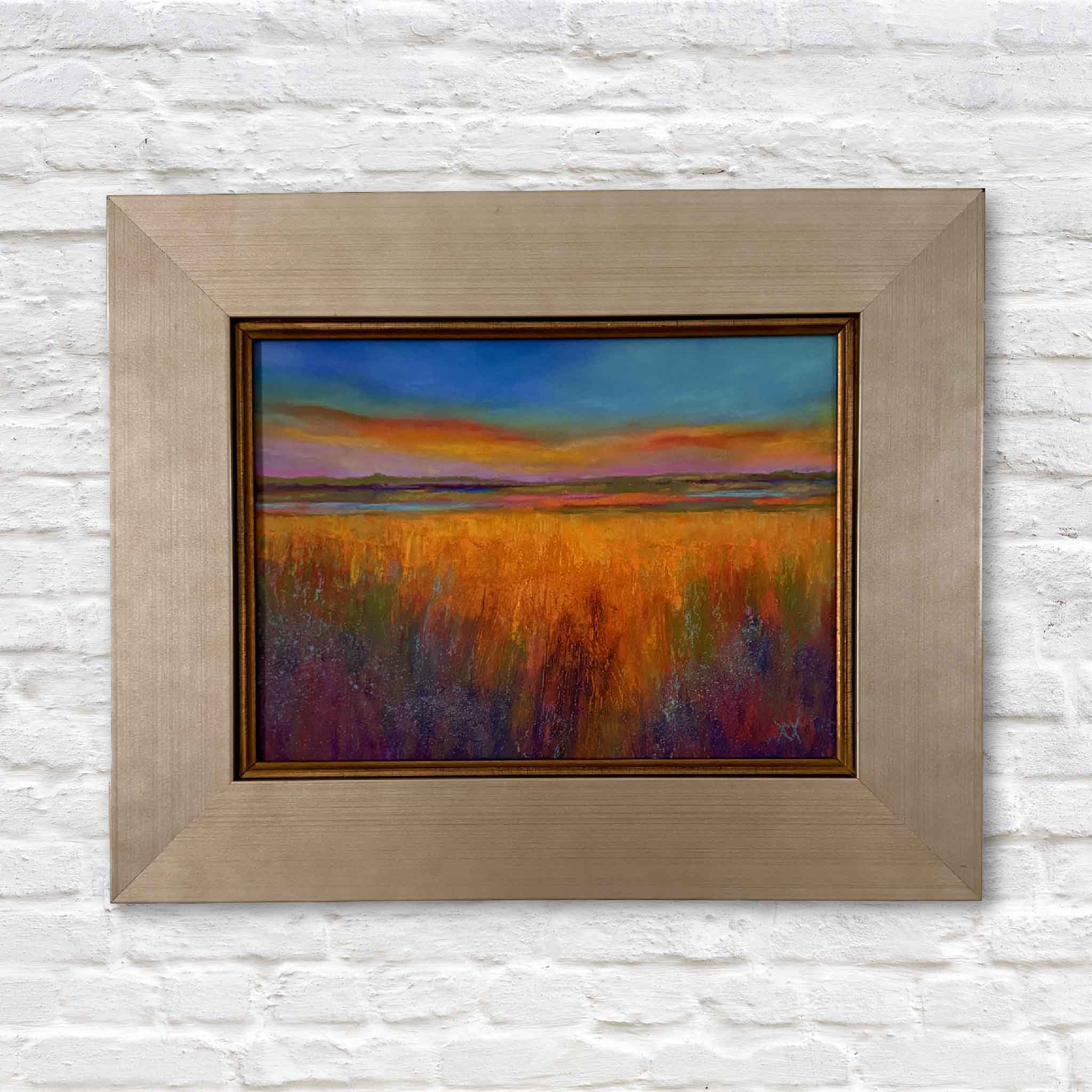 Original pastel landscape titled The Golden Hour by Vida Miller, depicting a glowing Lowcountry marsh at sunset with vibrant gold, orange, purple, and blue tones, shown framed and ready to hang. Shown at Gray Man Gallery.