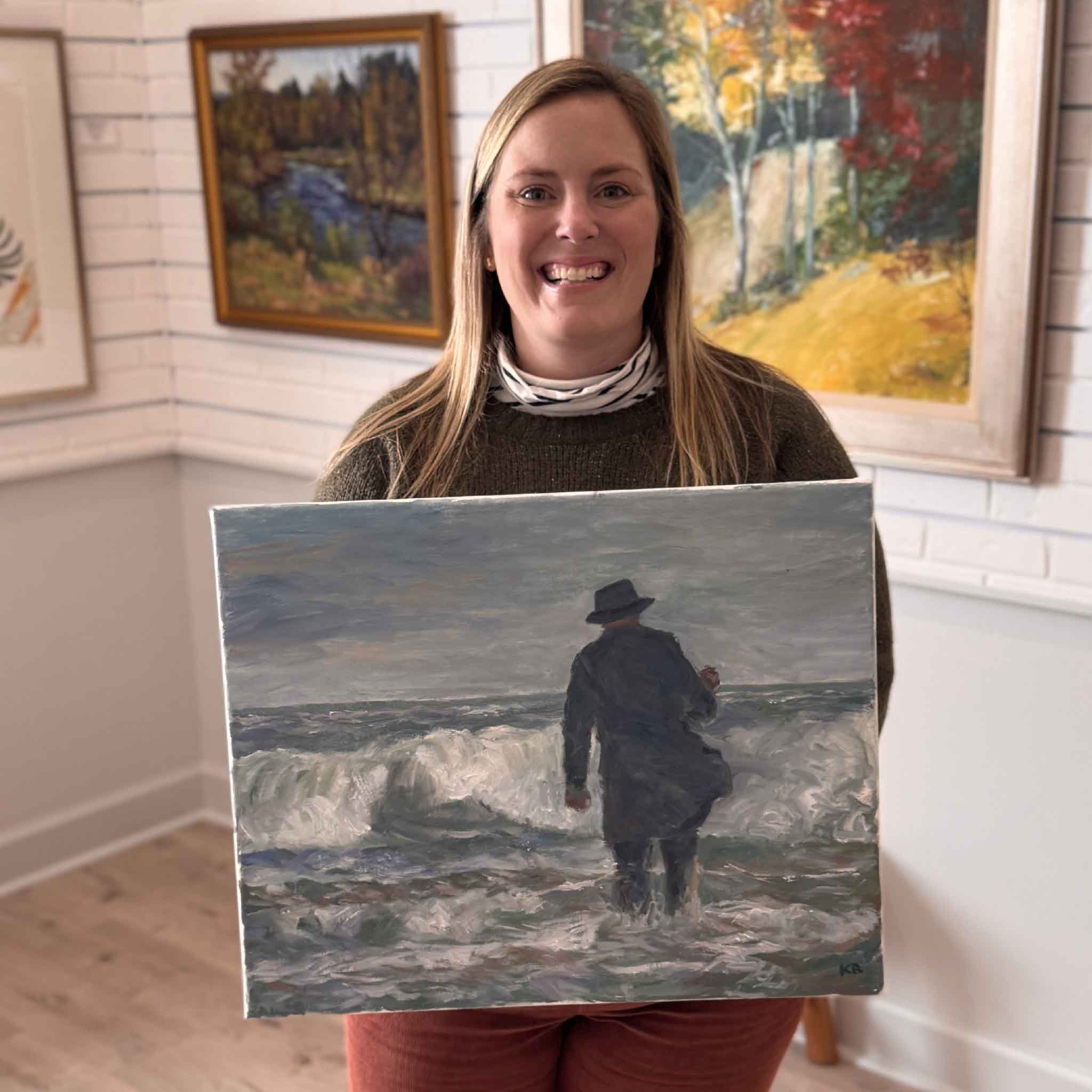 Bordy holding Gray Man I original oil painting by local artist Kathy Robinson inside Gray Man Gallery in Pawleys Island showing scale of coastal South Carolina artwork inspired by the Gray Man legend