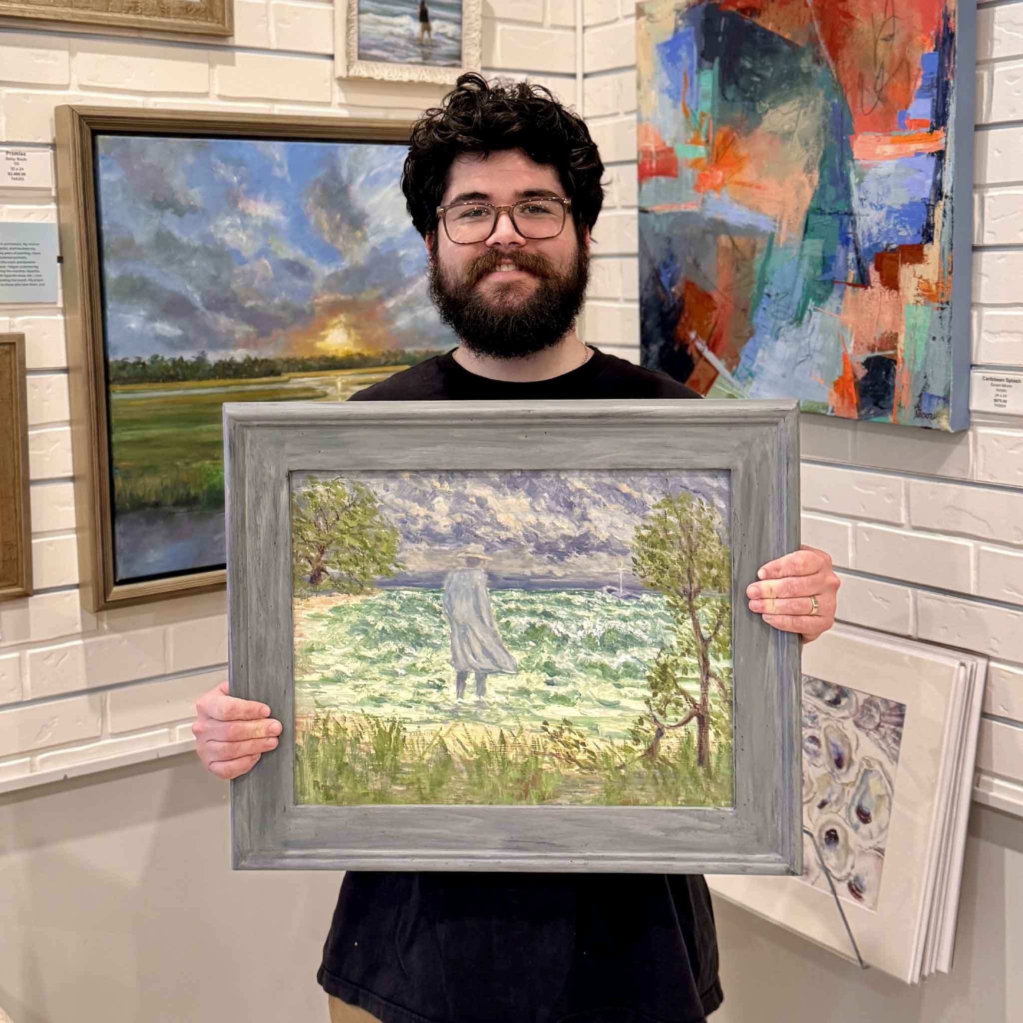 Peyton holding “The Gray Man Returns” original oil painting by Michael Rogan at Gray Man Gallery, showing the Pawleys Island legend against a stormy coastal backdrop.
