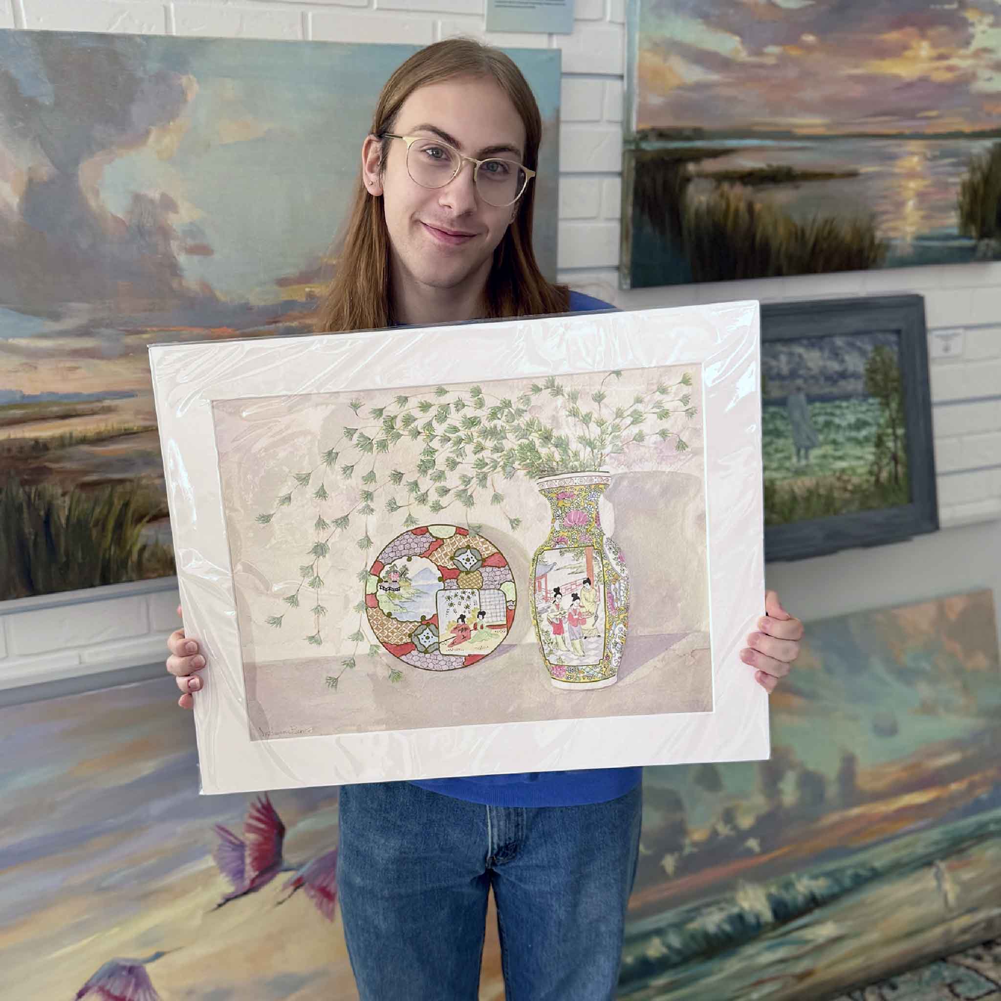 A Gray Man Gallery team member holds Hanging Bamboo Geisha by Mimi Beaver, an original watercolor featuring a decorative vase, plate, and cascading bamboo, donated to benefit Salty Dogs Senior Animal Rescue.