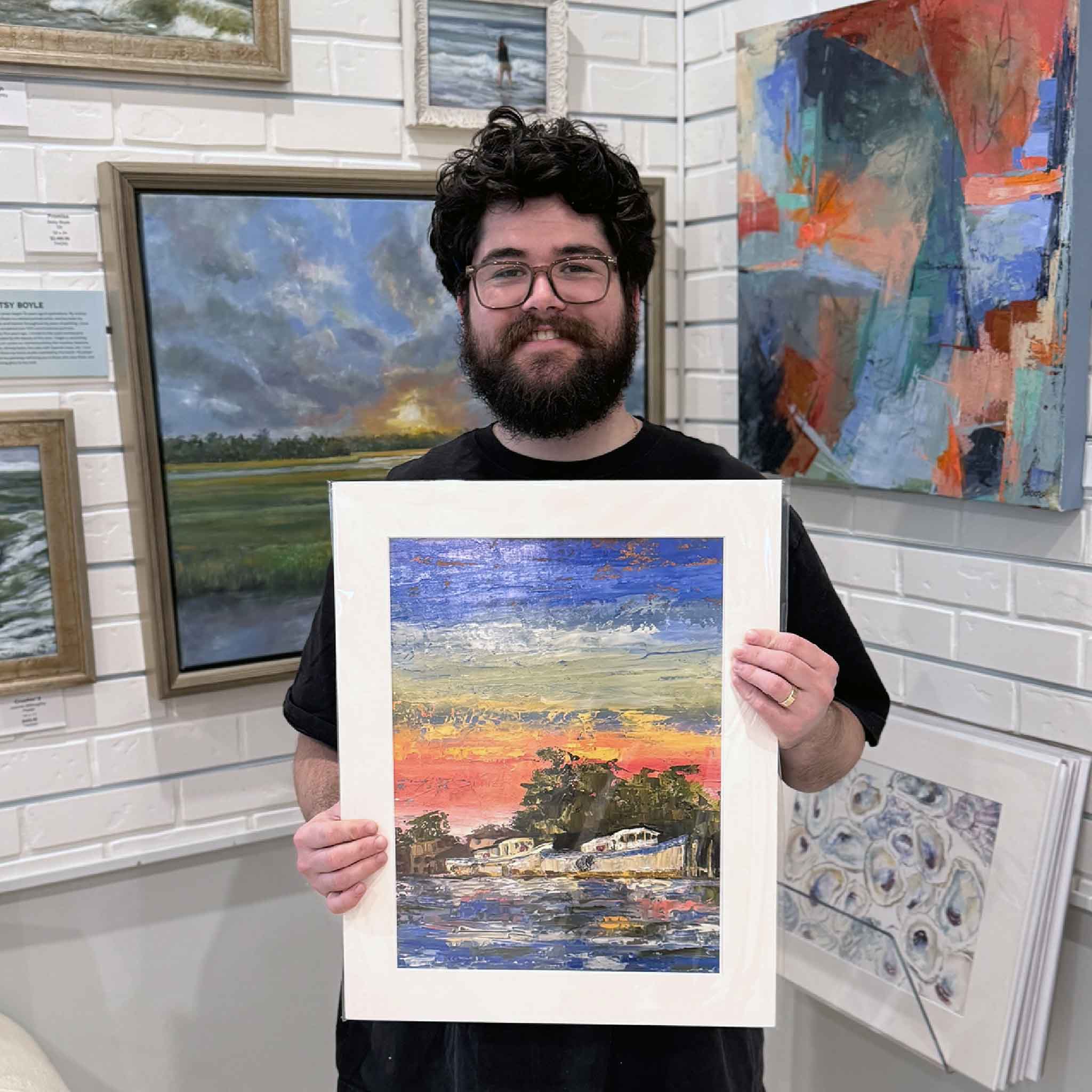 Team member holding Jeanne O’Neal’s “Harbor Sunset” giclée print, matted to a standard 16x20 size, featuring a vibrant Lowcountry harbor scene at dusk.