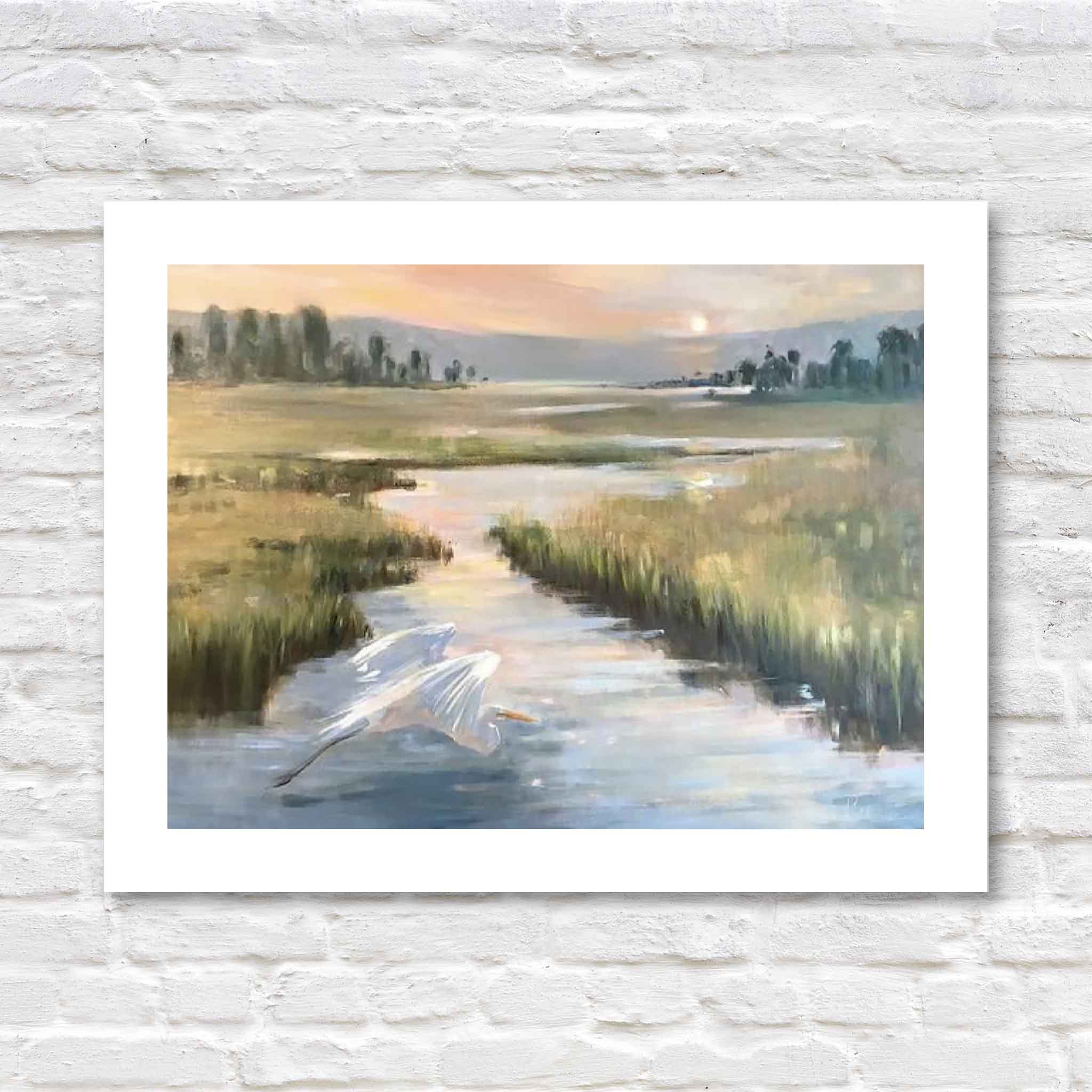 “Coming Home” 16x12 giclée print by Helli Luck featuring an egret gliding over a sunset marsh, matted in white against a brick backdrop.