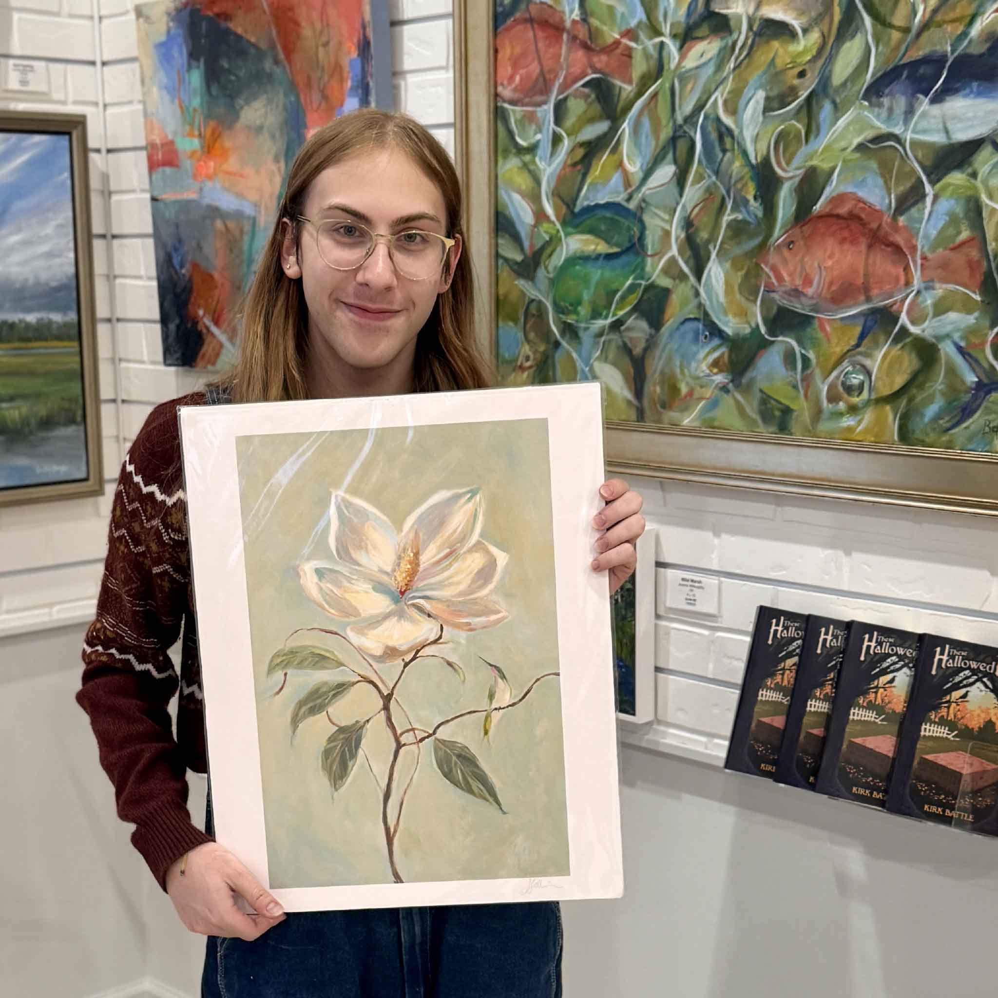 A gallery staff member holds Helli Luck’s 16x20 Southern Charm magnolia print, showing the artwork’s delicate petals and elegant Southern palette.