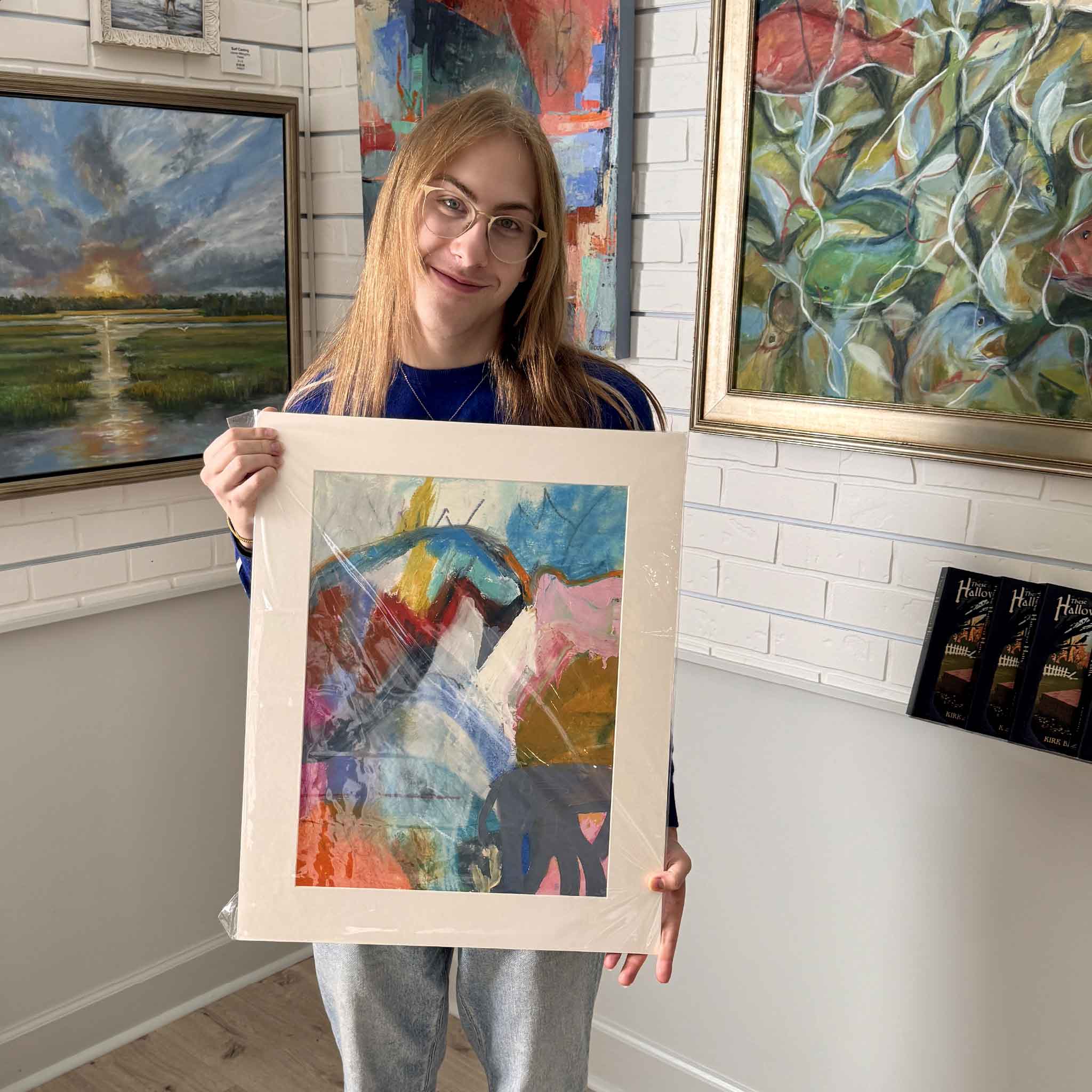 This image shows a Gray Man Gallery employee holding Caroline Young's original mixed-media piece High Tide, highlighting the artwork’s bright abstract palette and standard 18x24 matted presentation.