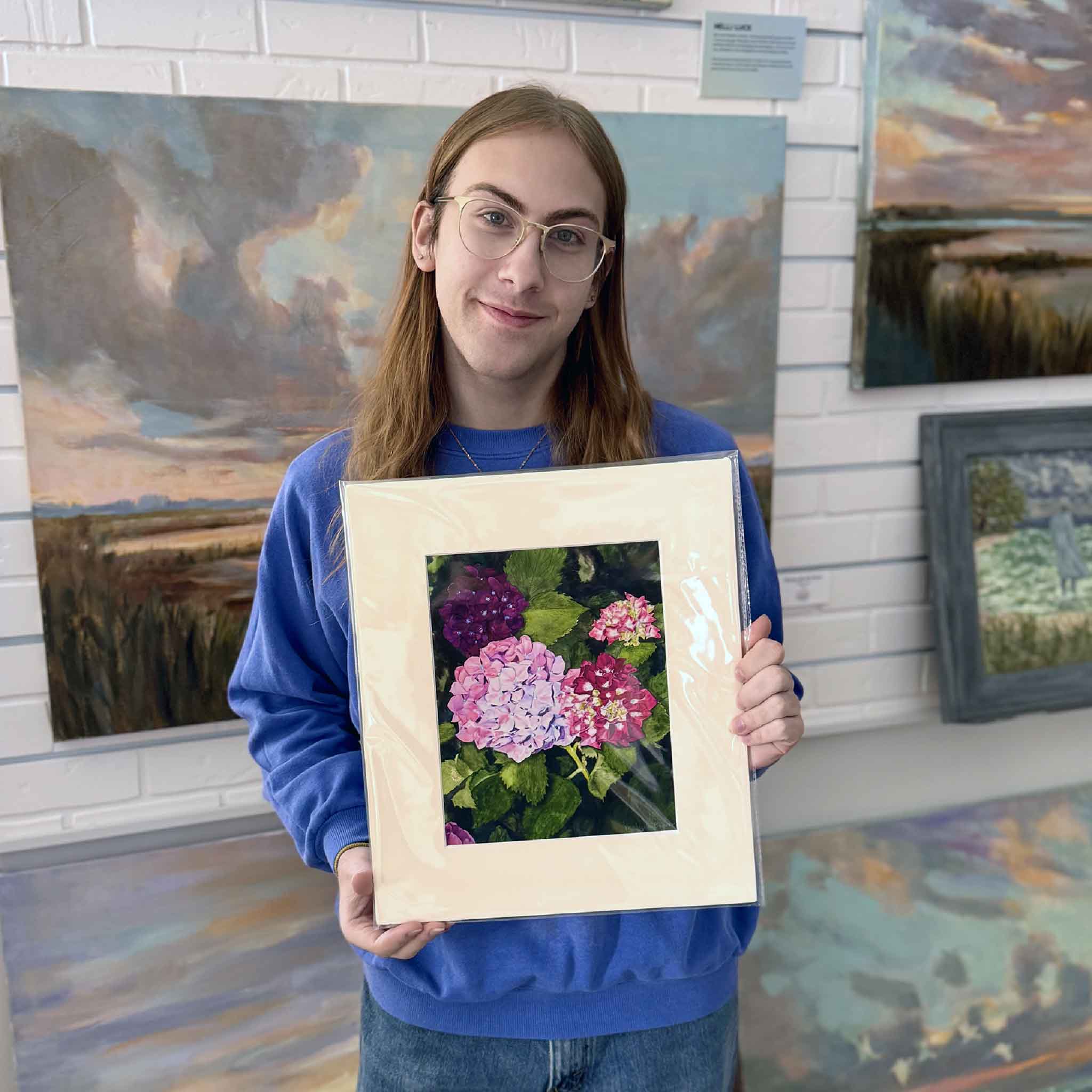 A Gray Man Gallery team member holds Hydrangea 1 by Mimi Beaver, an original watercolor artwork donated in full support of Salty Dogs Senior Animal Rescue, with all proceeds benefiting senior dogs.