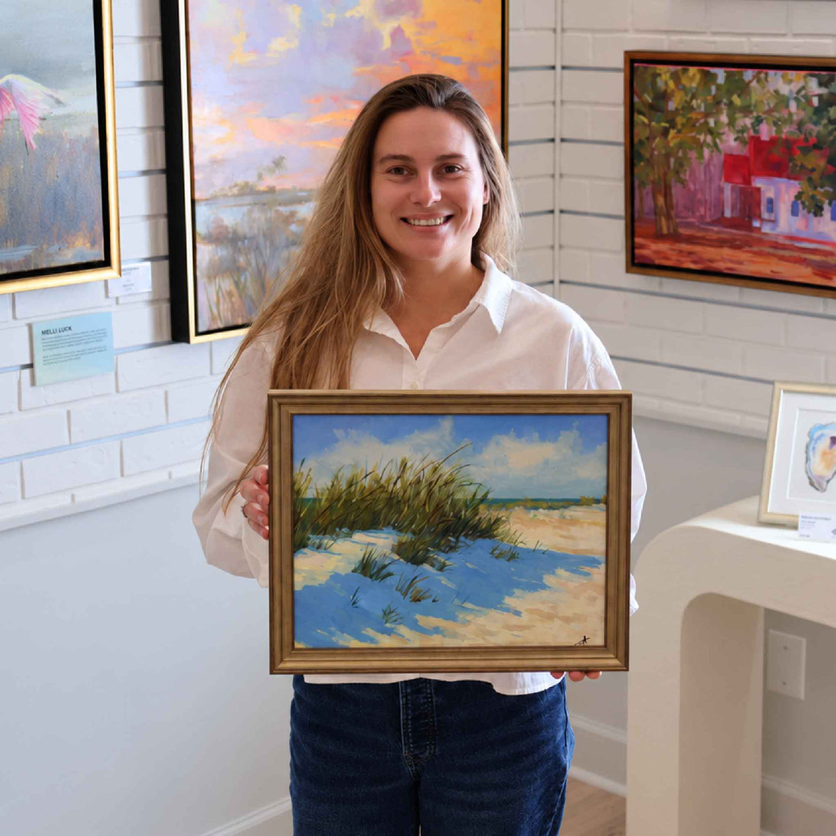 Gray Man Gallery team member holding Dune Shadows, an original coastal oil painting by local artist Jamie Arnold, for scale inside the Pawleys Island gallery.