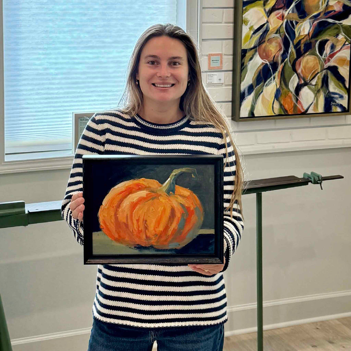 Gray Man Gallery team member holding Lil’ Punkin, a framed original oil pumpkin painting by local artist Jamie Arnold, for scale inside the Pawleys Island gallery.