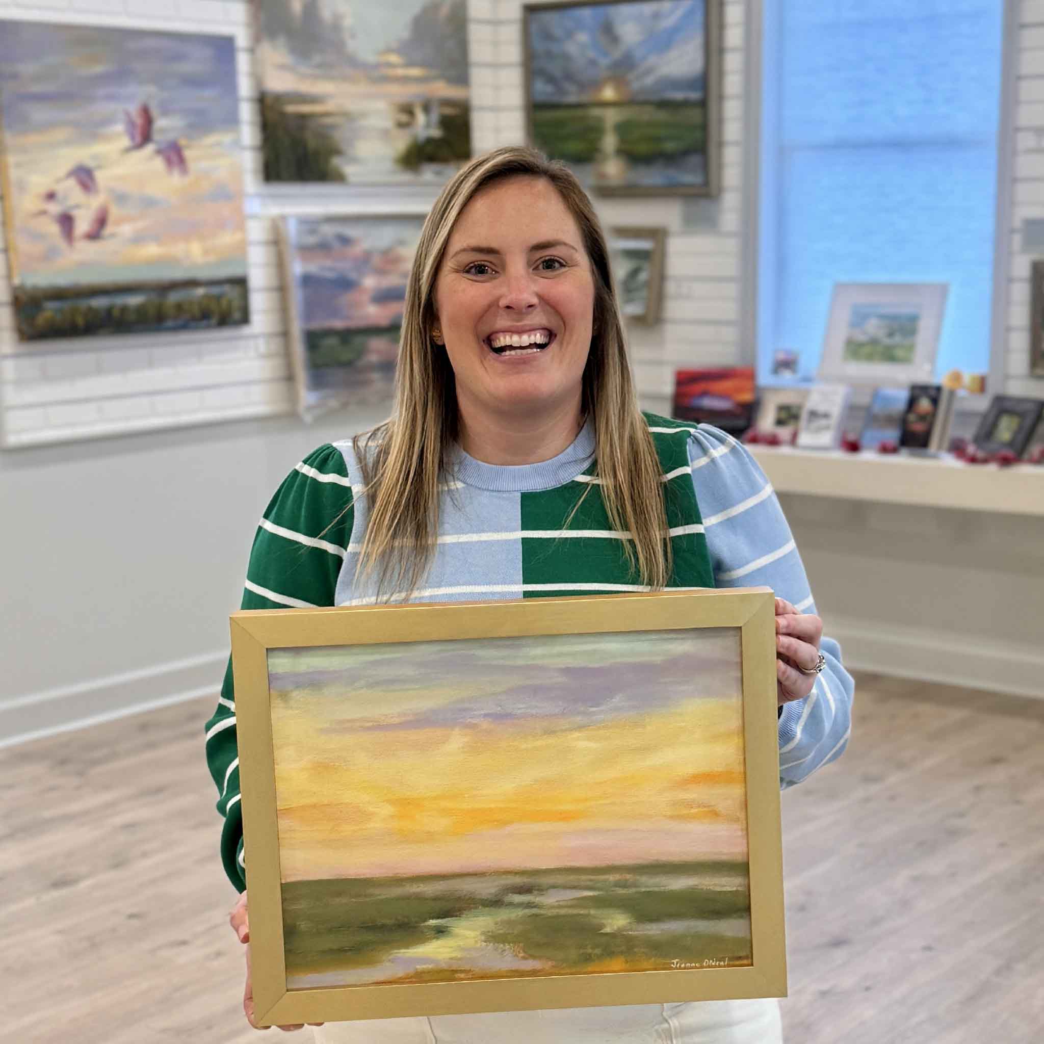 Bordy holding “2 A.M.” by Jeanne O’Neal, original oil painting of a Lowcountry marsh at night with soft gold and lavender sky, framed in signature gold frame at Gray Man Gallery in Pawleys Island South Carolina