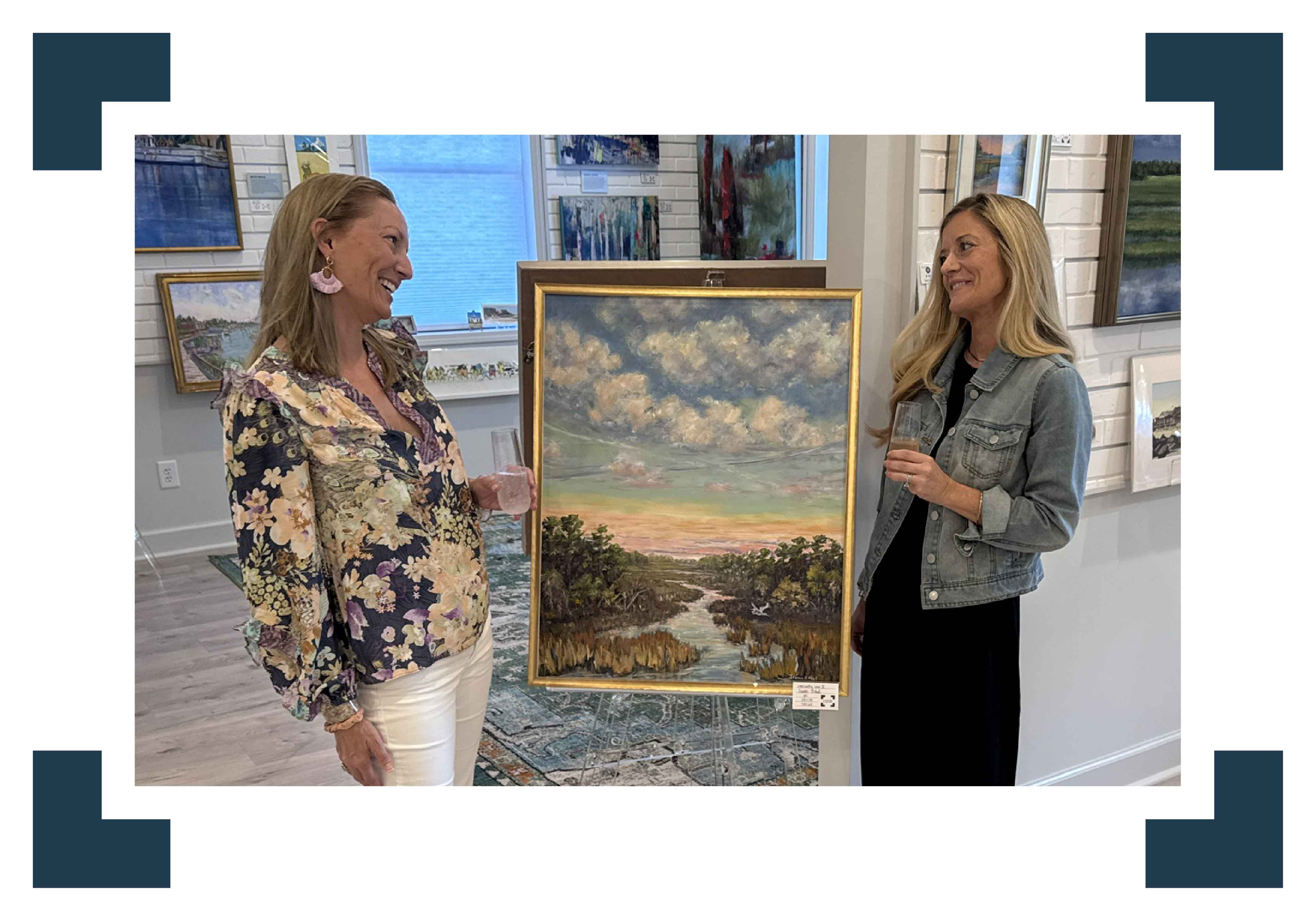 Jeanne O’Neal, established Lowcountry artist, stands inside Gray Man Gallery in Pawleys Island, South Carolina, presenting a framed original marsh landscape oil painting. The image captures the welcoming interior of the long-standing local art gallery, highlighting its commitment to exhibiting regional artists, original fine art, and thoughtfully curated coastal artwork inspired by South Carolina’s marshlands and waterways.