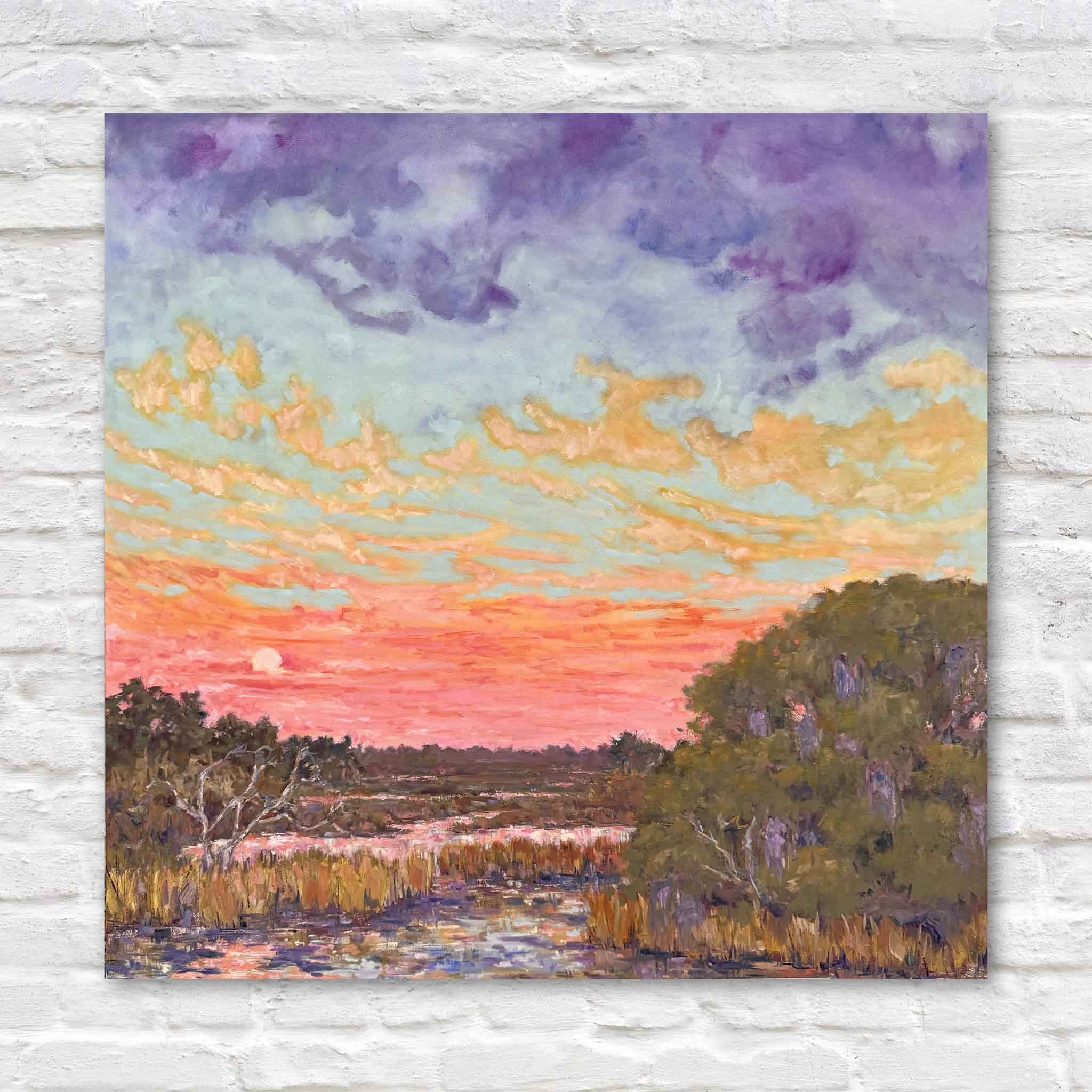 Hugs & Kisses Afterglow by Jeanne O’Neal displayed on a white wall, a large original Lowcountry oil painting of a sunset marsh scene with luminous coral and peach skies, lavender clouds, and reflective tidal water, showcasing expressive brushwork and soft romantic color palette typical of Pawleys Island local artist work at Gray Man Gallery.