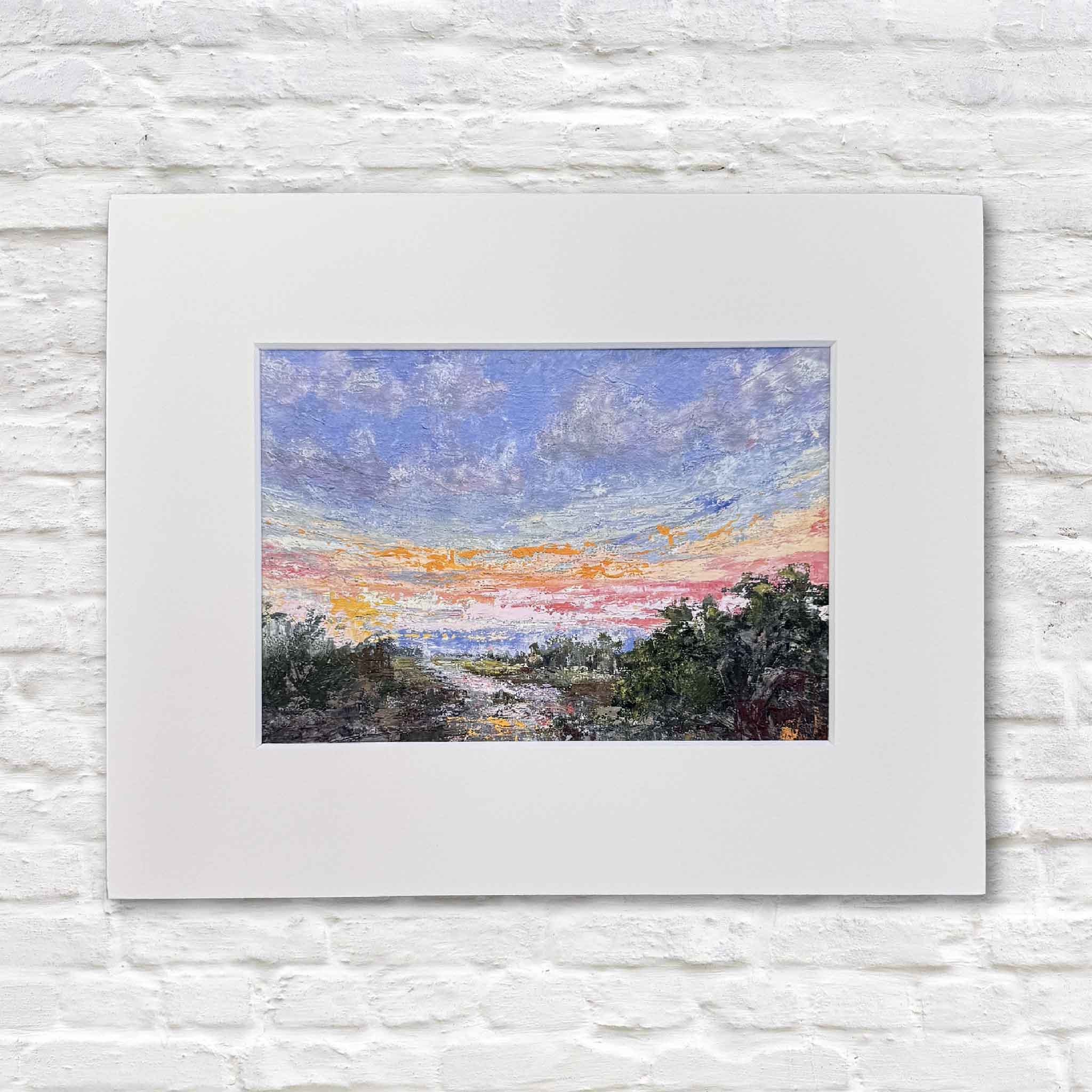 Marshlight fine art giclée print by local South Carolina artist Jeanne O’Neal professionally matted to fit a standard 8x10 frame, shown on white brick wall at Gray Man Gallery in Pawleys Island, capturing glowing coral and gold sunset light over a coastal marsh landscape in painterly detail