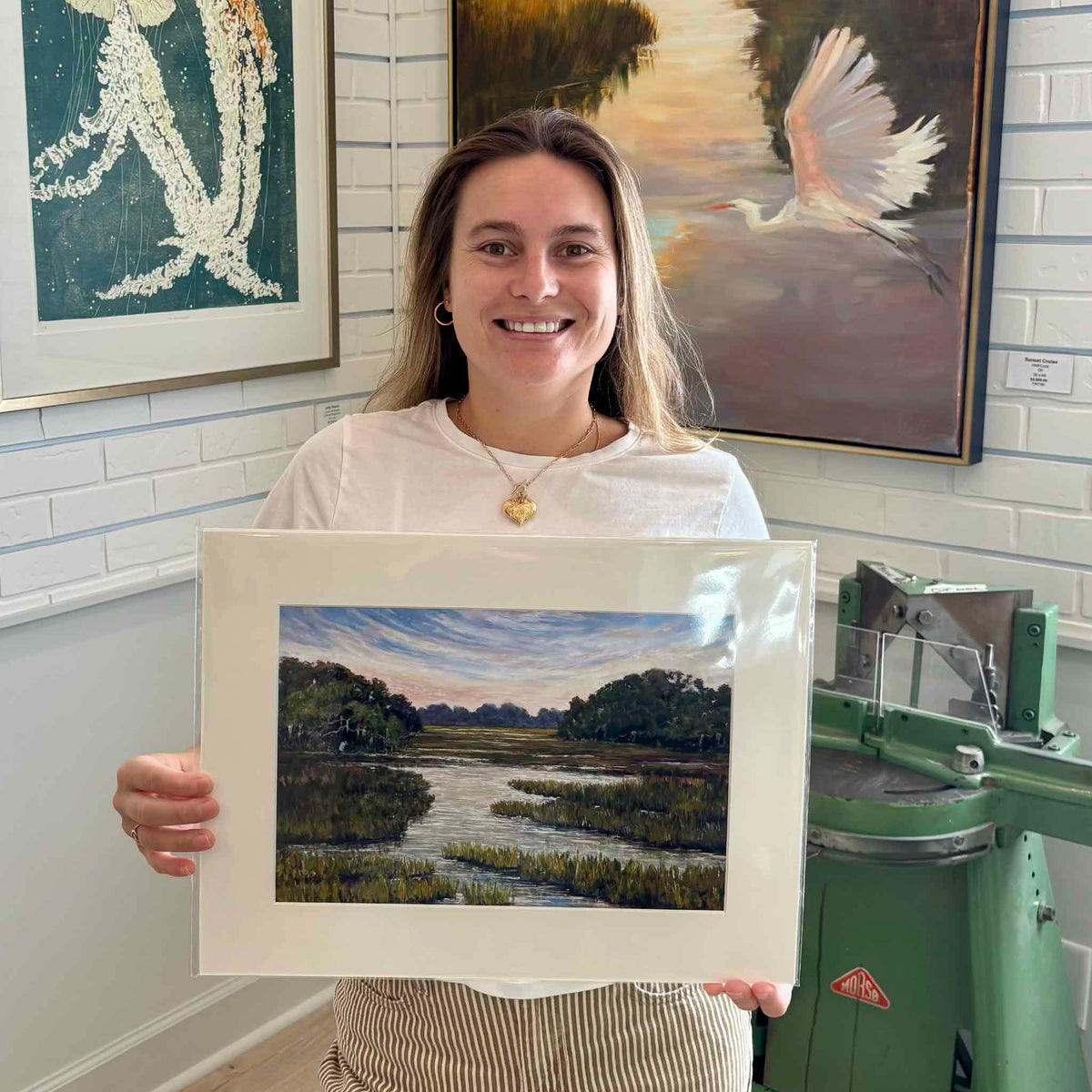 Gray Man Gallery team member holding The Way Home, a matted fine art giclée print by local artist Jeanne O’Neal featuring a peaceful South Carolina Lowcountry marsh and tidal creek, shown for scale at Gray Man Gallery in Pawleys Island.