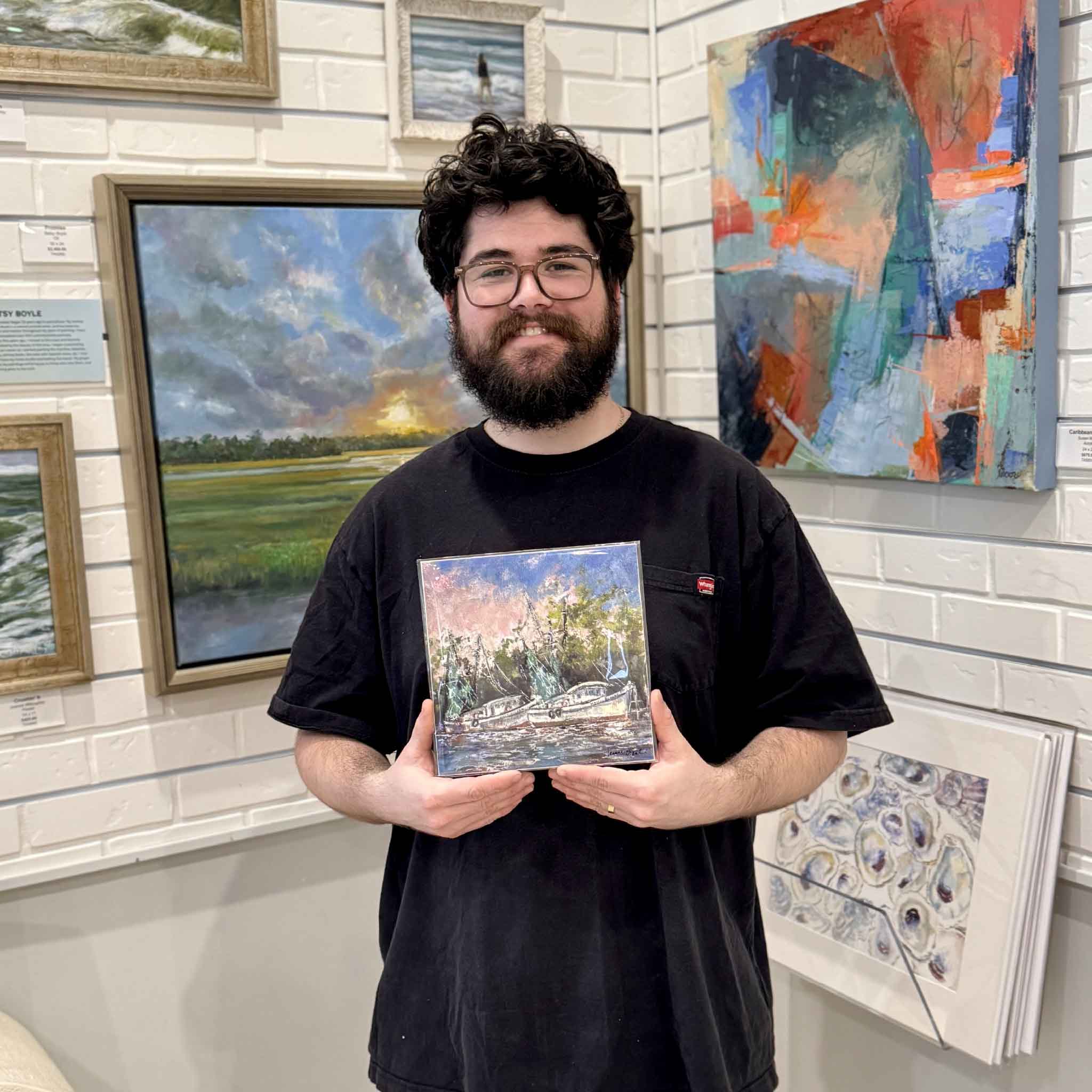 Gallery team member holding the Evening Light 8x8 coastal print by Lowcountry artist Jeanne O’Neal inside Gray Man Gallery, surrounded by local artwork.