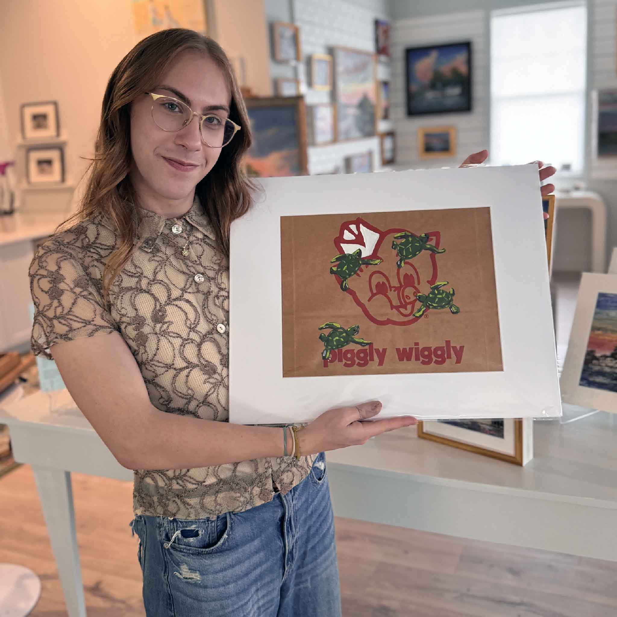 Jenny Reynolds’ “Piggly Wiggly: Turtles” painting on a recycled Piggly Wiggly grocery bag, featuring the classic pig logo surrounded by playful green turtles.