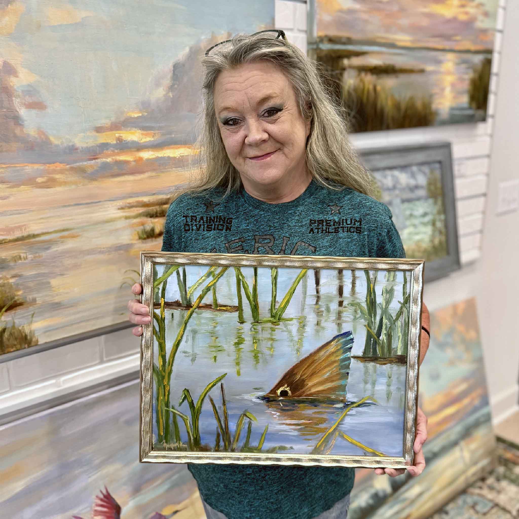 GMG team member holding Spottail in the Marsh by Jenny Reynolds to show the scale of the framed original oil painting.