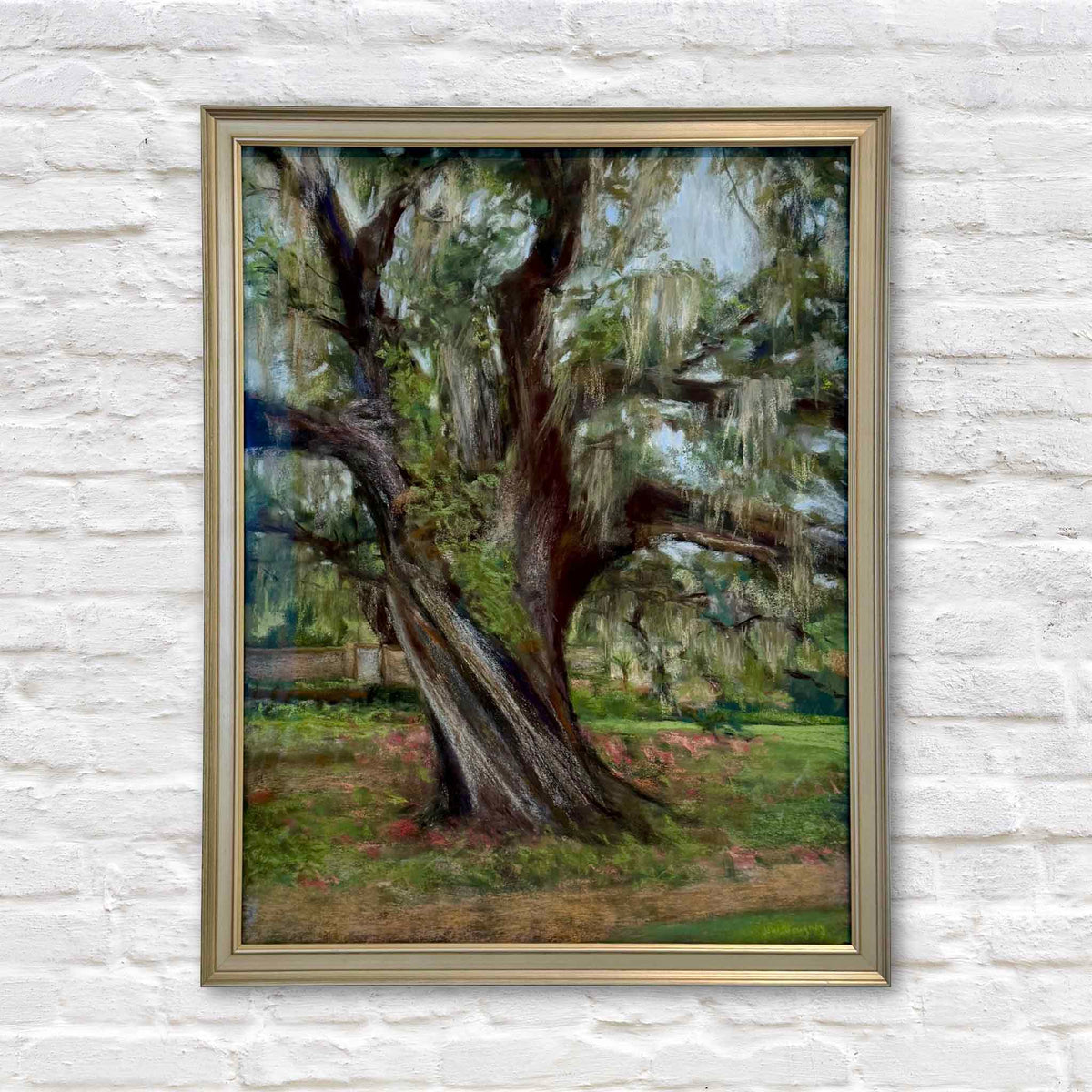 Nature's Majesty, an original pastel painting by local South Carolina artist Joanne Willoughby, depicting a magnificent live oak tree at Brookgreen Gardens in Murrells Inlet, South Carolina. The detailed Southern landscape features a massive twisting trunk, sprawling branches, cascading Spanish moss, and lush green foliage. Presented in a champagne-gold frame against a white brick wall at Gray Man Gallery in Pawleys Island, South Carolina.