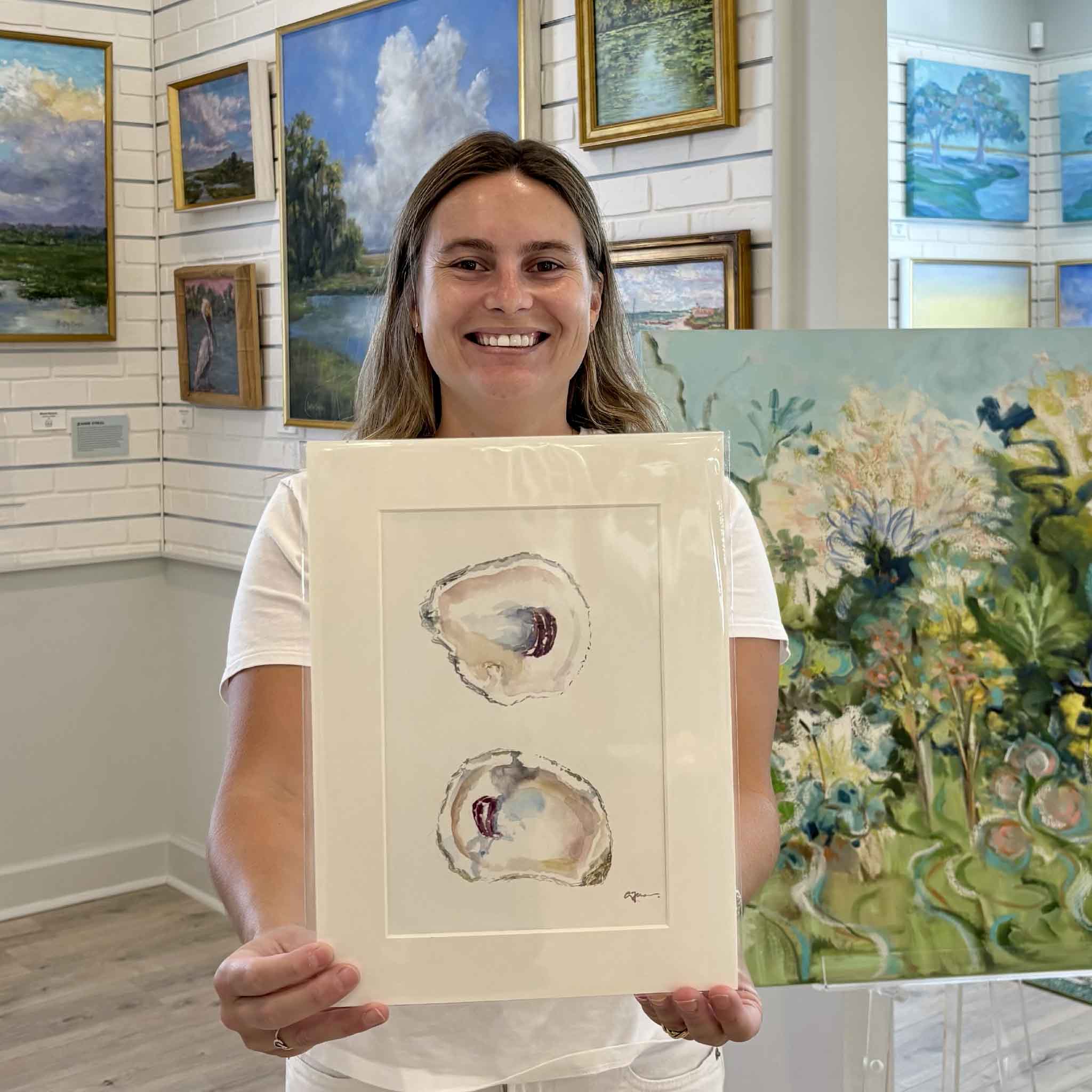 Kyra holding "Surprise," an original oyster watercolor by Allison Farr from her Lowcountry Jewels series inside Gray Man Gallery in Pawleys Island, South Carolina. The professionally matted original artwork features two delicately painted oyster shells and is ready to fit any standard 9x12 frame.