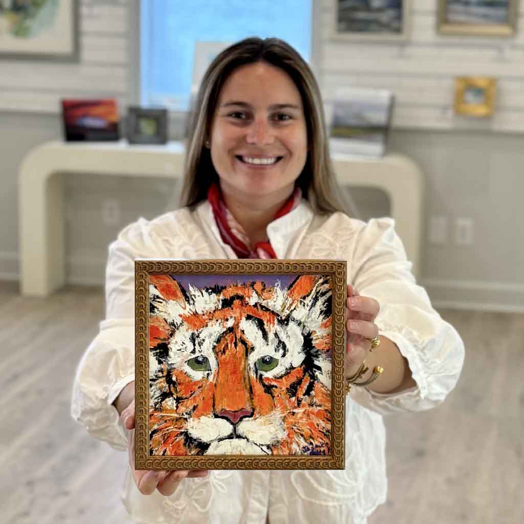 Kyra holding Confidence, an original Clemson Tiger oil painting by local artist Jeanne O'Neal. Framed wildlife artwork featuring vibrant orange and purple colors at Gray Man Gallery in Pawleys Island, South Carolina.