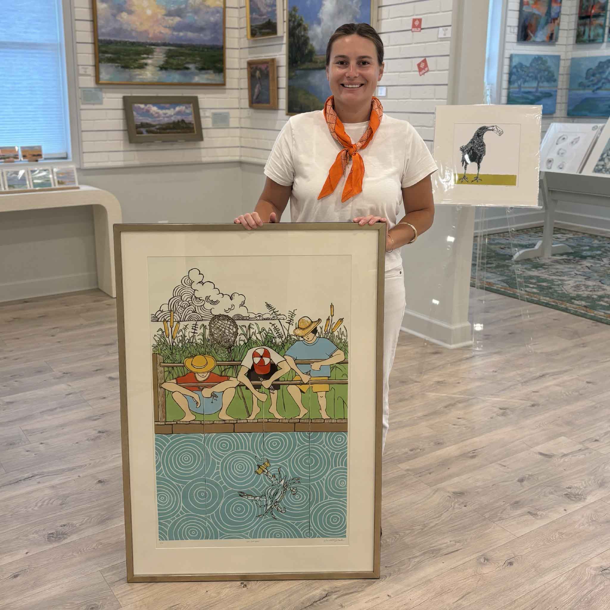 Kyra displays "Git Da' Net," Laurie Brownell McIntosh's award-winning reduction linocut, at Gray Man Gallery in Pawleys Island, South Carolina. The framed artwork captures a nostalgic Lowcountry crabbing scene and demonstrates the scale of this celebrated First Place South Carolina State Fair winner.