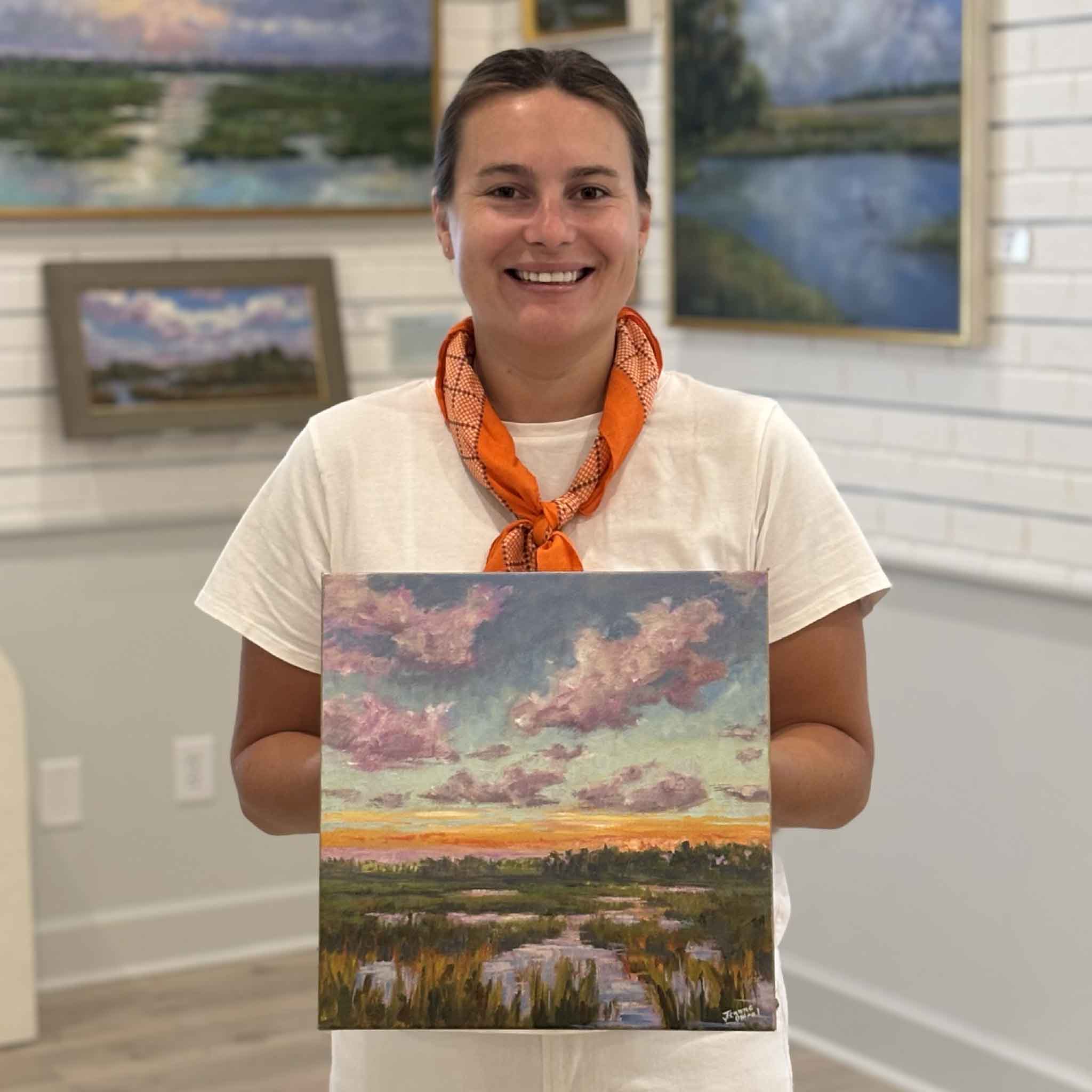 Gray Man Gallery team member Kyra holding After Sunset by Jeanne O'Neal to show scale, an original gallery wrapped oil painting featuring a colorful Lowcountry marsh sunset and winding tidal creek.