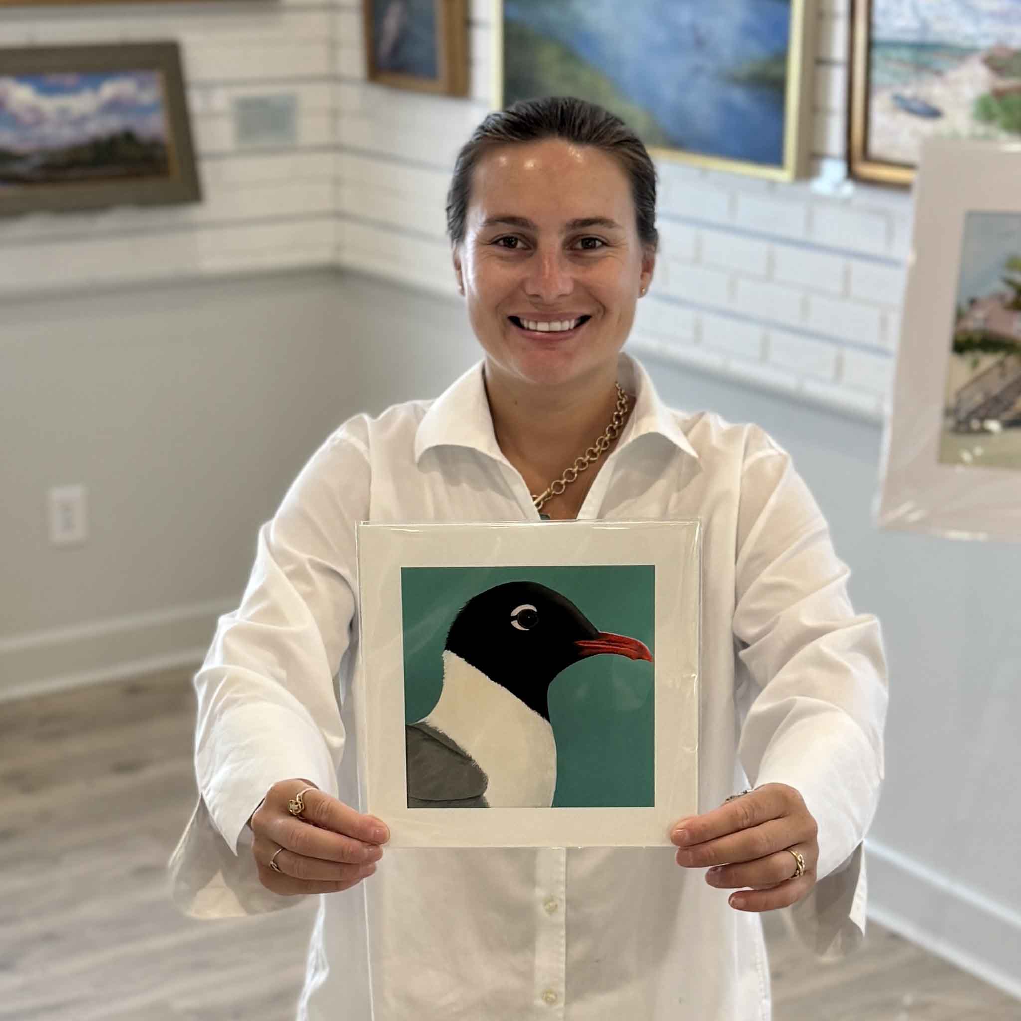Kyra holds Laughing Gull, an 8×8 bird print by Georgetown, South Carolina local artist Nancy Jones Lowe at Gray Man Gallery in Pawleys Island. Printed on premium 100% cotton archival fine art paper with archival pigment inks, this colorful coastal bird print fits any standard 8×8 frame without custom framing.