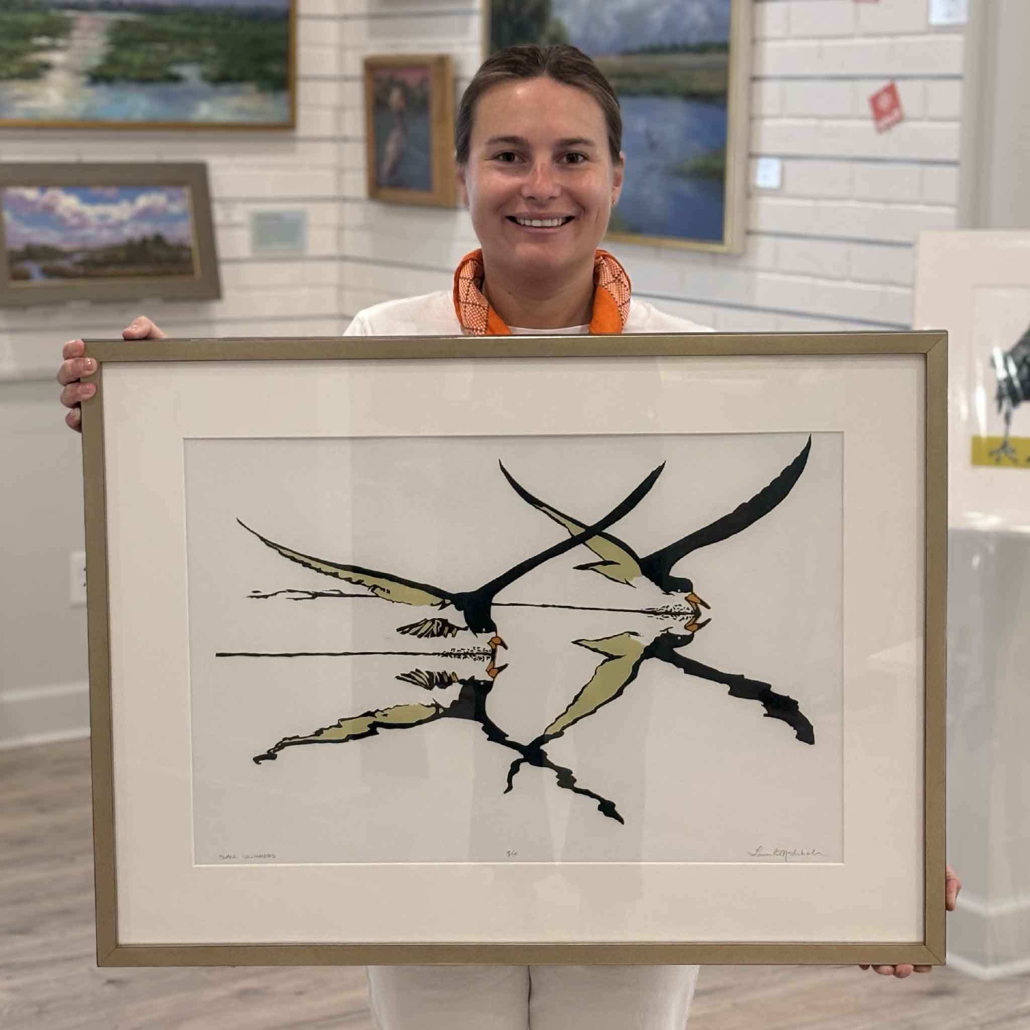 Kyra holding Black Skimmers by Laurie Brownell McIntosh at Gray Man Gallery in Pawleys Island, South Carolina, showing the scale of the original framed reduction linocut depicting black skimmers in flight above their reflections.