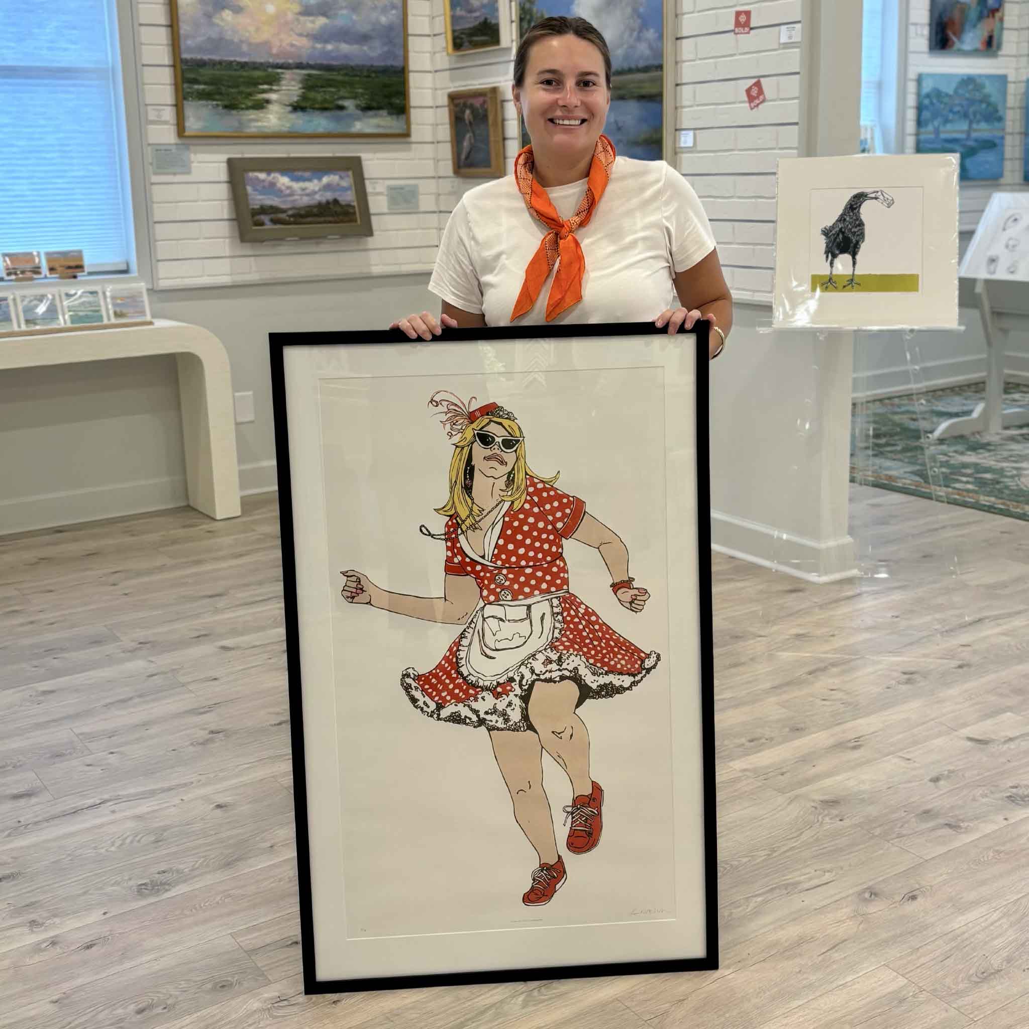Kyra holding Mande Milkshaker by Laurie Brownell McIntosh at Gray Man Gallery in Pawleys Island, South Carolina, showing the scale of the original oil reduction linocut featuring a dancing Mande Milkshaker in a red polka-dot dress, professionally matted and framed.