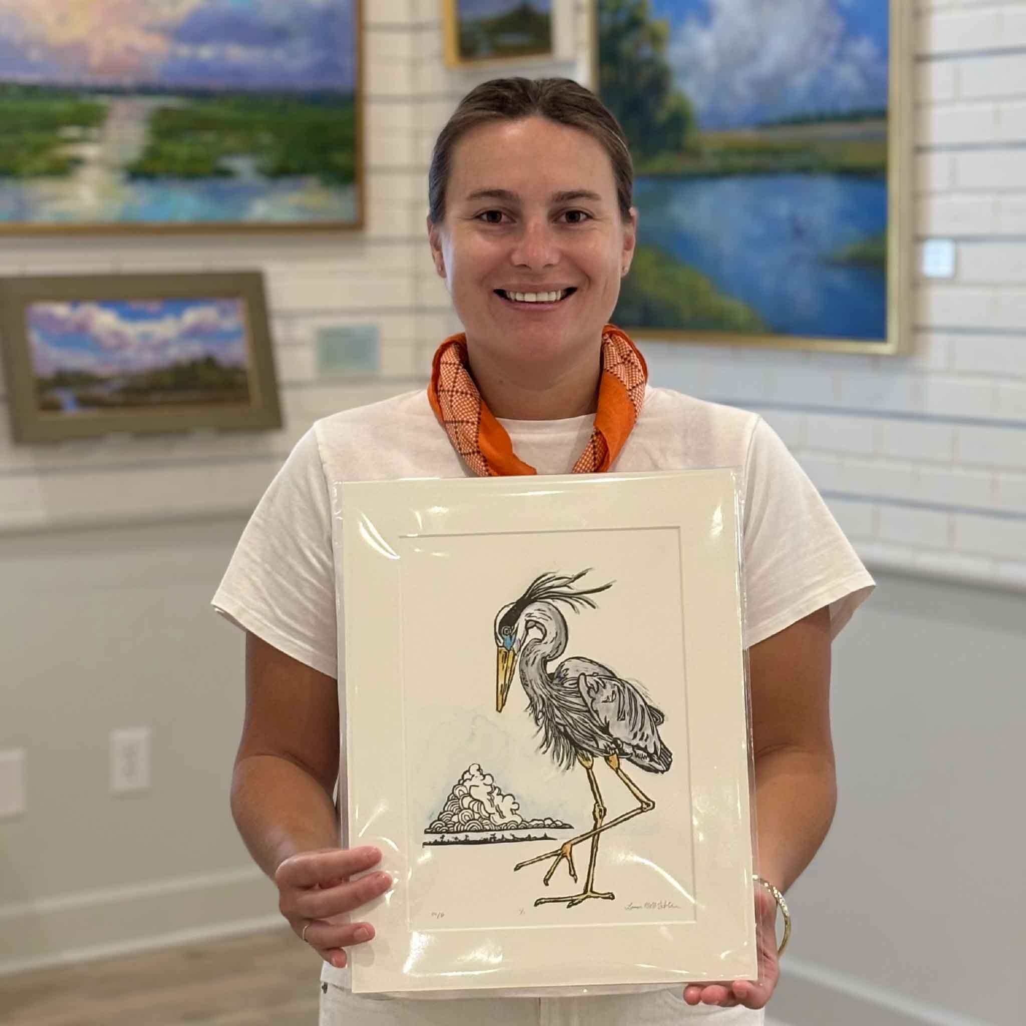 Kyra holding Laurie McIntosh's Blue Heron original monoprint at Gray Man Gallery in Pawleys Island, South Carolina. The image shows the scale of this one-of-a-kind artwork, matted to fit a standard 11x14 frame.