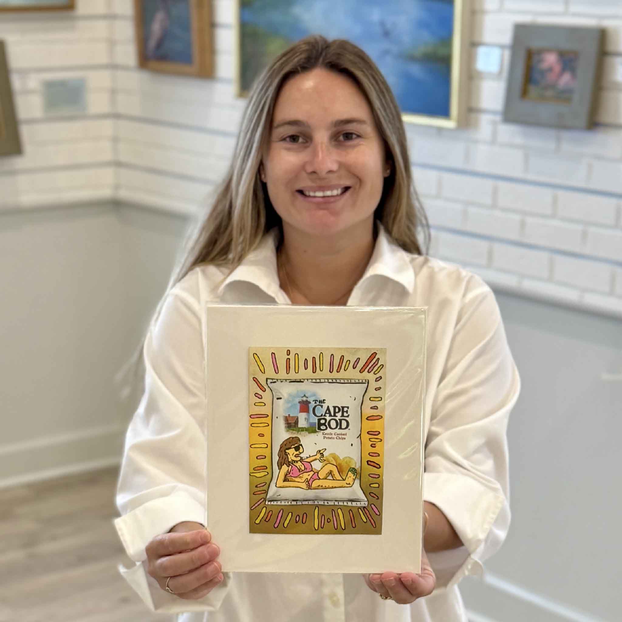 Kyra holds Cape Bod Pink by Charleston artist Nick Kawczynski at Gray Man Gallery in Pawleys Island, South Carolina. This one-of-a-kind mixed media artwork is painted on a reclaimed Cape Cod potato chip box and professionally matted to fit a standard 8x10 frame, making it easy to display without custom framing.