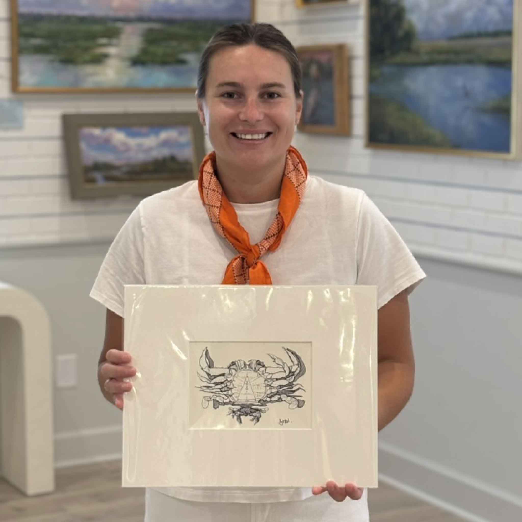 Gray Man Gallery team member Kyra holding Blue Crab by Todd Halamka to show scale, a professionally matted pen-and-ink coastal print featuring one of the South Carolina coast's most iconic marine species.