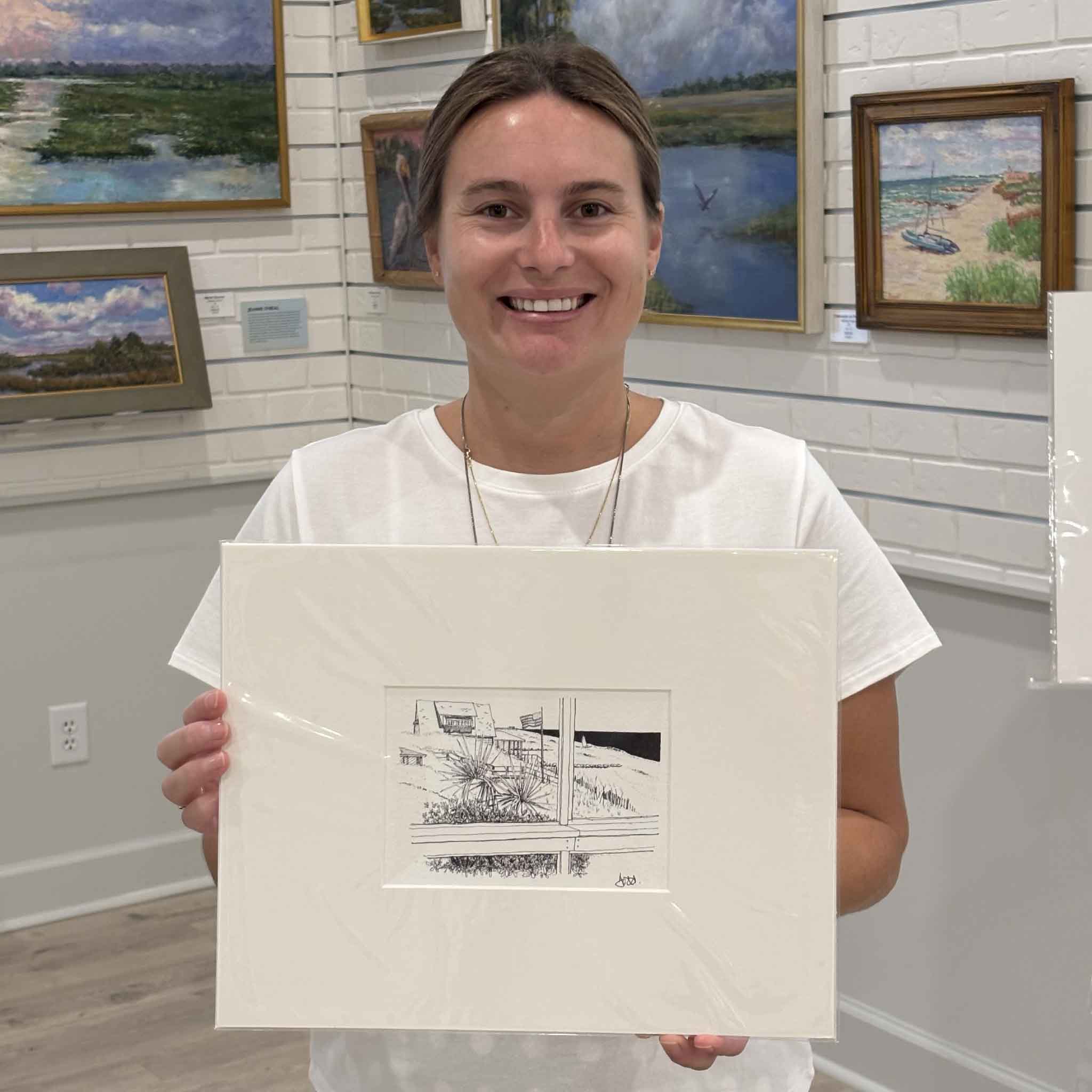 Kyra holds Todd Halamka's Fourth of July at Pawleys print inside Gray Man Gallery in Pawleys Island, South Carolina. Professionally matted to a standard 11x14 size, this detailed pen-and-ink print features a classic Pawleys Island beach house, sea oats, dunes, and an American flag, fitting any standard 11x14 ready-made frame.