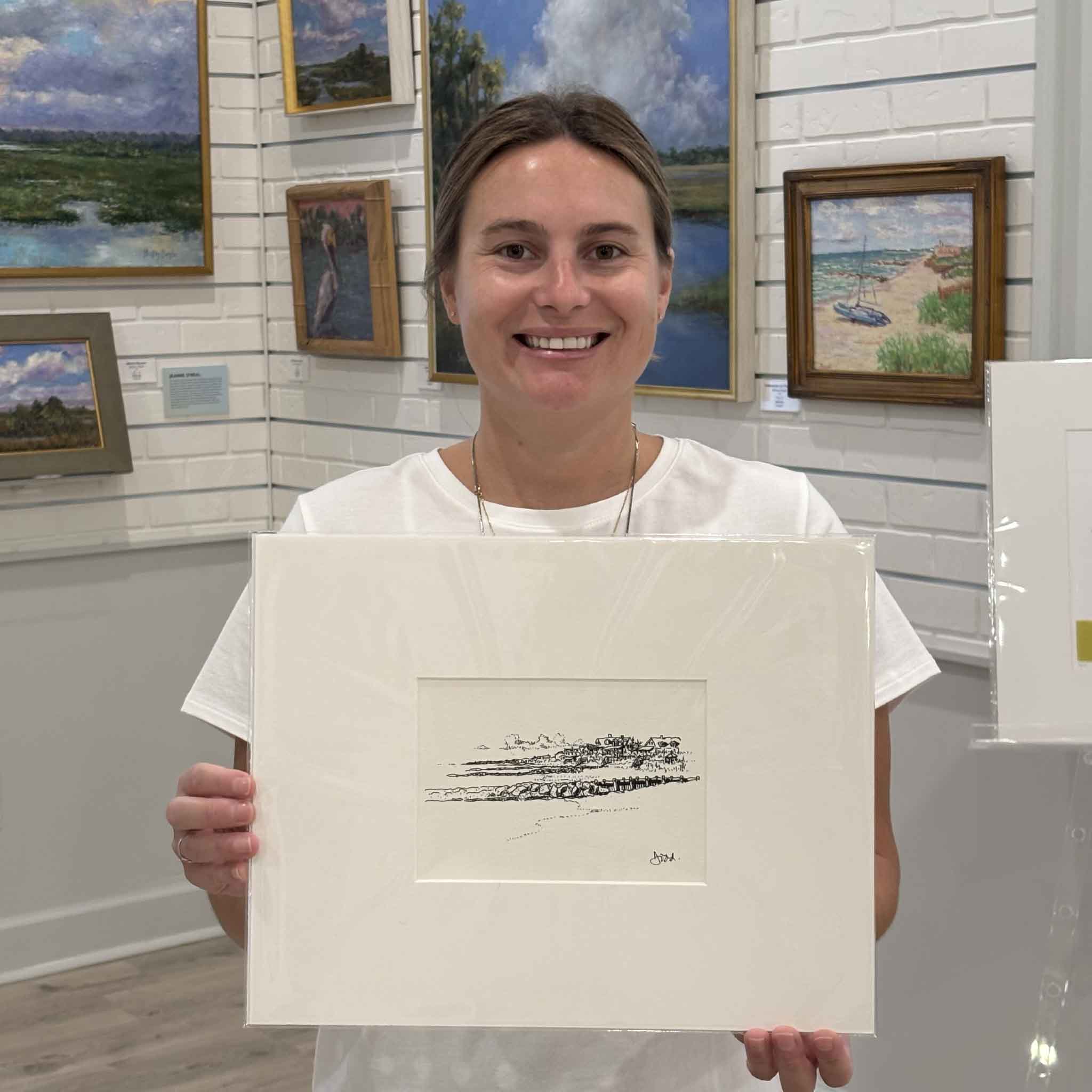 Kyra holds Todd Halamka's Pawleys Island Looking South print inside Gray Man Gallery in Pawleys Island, South Carolina. Professionally matted to a standard 11x14 size, this detailed pen-and-ink illustration features iconic Pawleys Island beach houses and coastal scenery and fits any standard 11x14 ready-made frame.